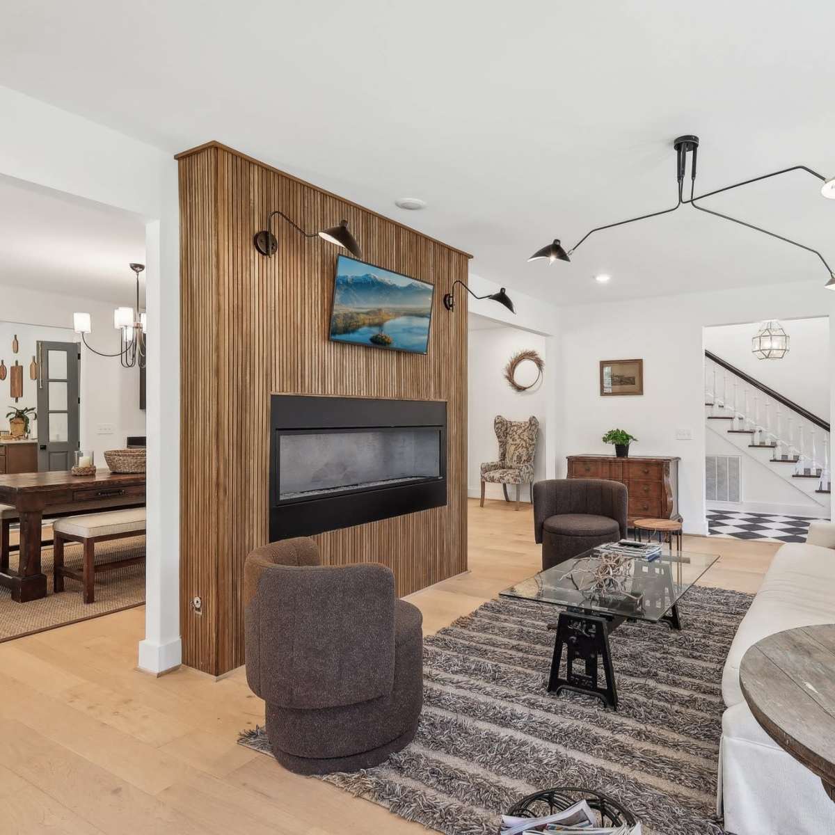 A modern living room with a fireplace, a glass coffee table, and a dining area in the background.