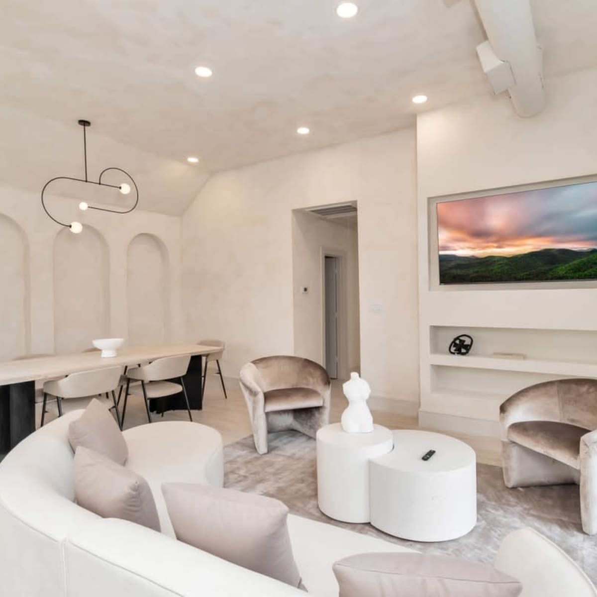 A modern, minimalist living space with a curved sofa, two armchairs, a coffee table, and a wall-mounted television.