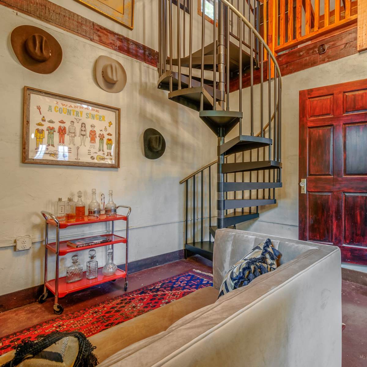 A small interior space featuring a spiral staircase, a red trolley with glass bottles, and a door leading to another room.