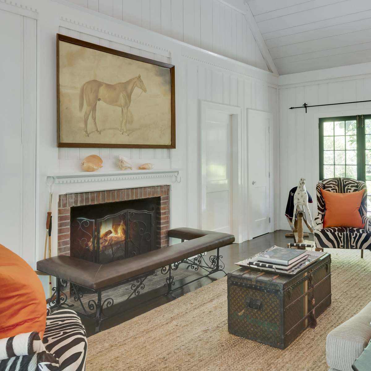 A cozy living room with a fireplace, a large painting of a horse on the wall, and various patterned furniture arranged around a woven rug.