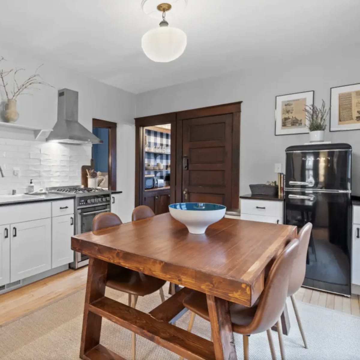 A modern kitchen features white cabinetry, stainless steel appliances, and a wooden dining table with brown chairs.