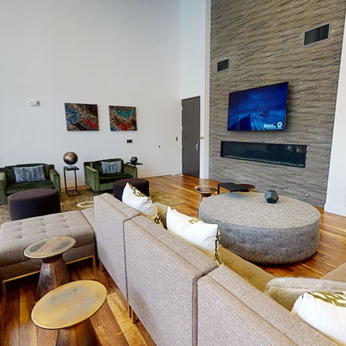 A modern living room with a large sectional sofa, a round coffee table, and a wall-mounted television above a stone fireplace.