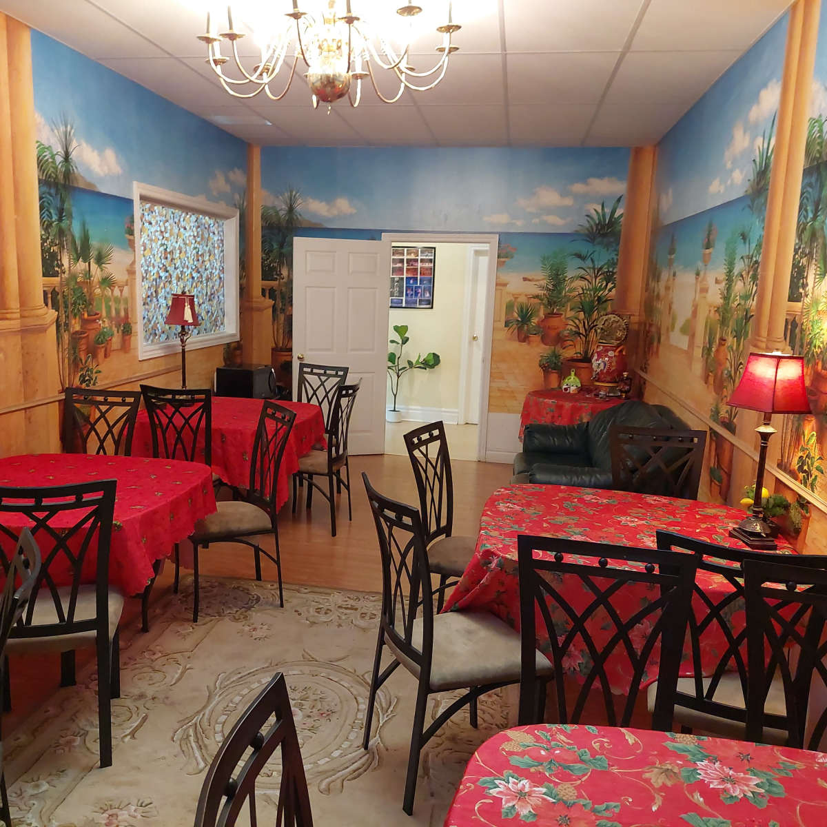 A dining area with red tablecloths and decorative lamps, set against a backdrop of painted tropical scenery on the walls.