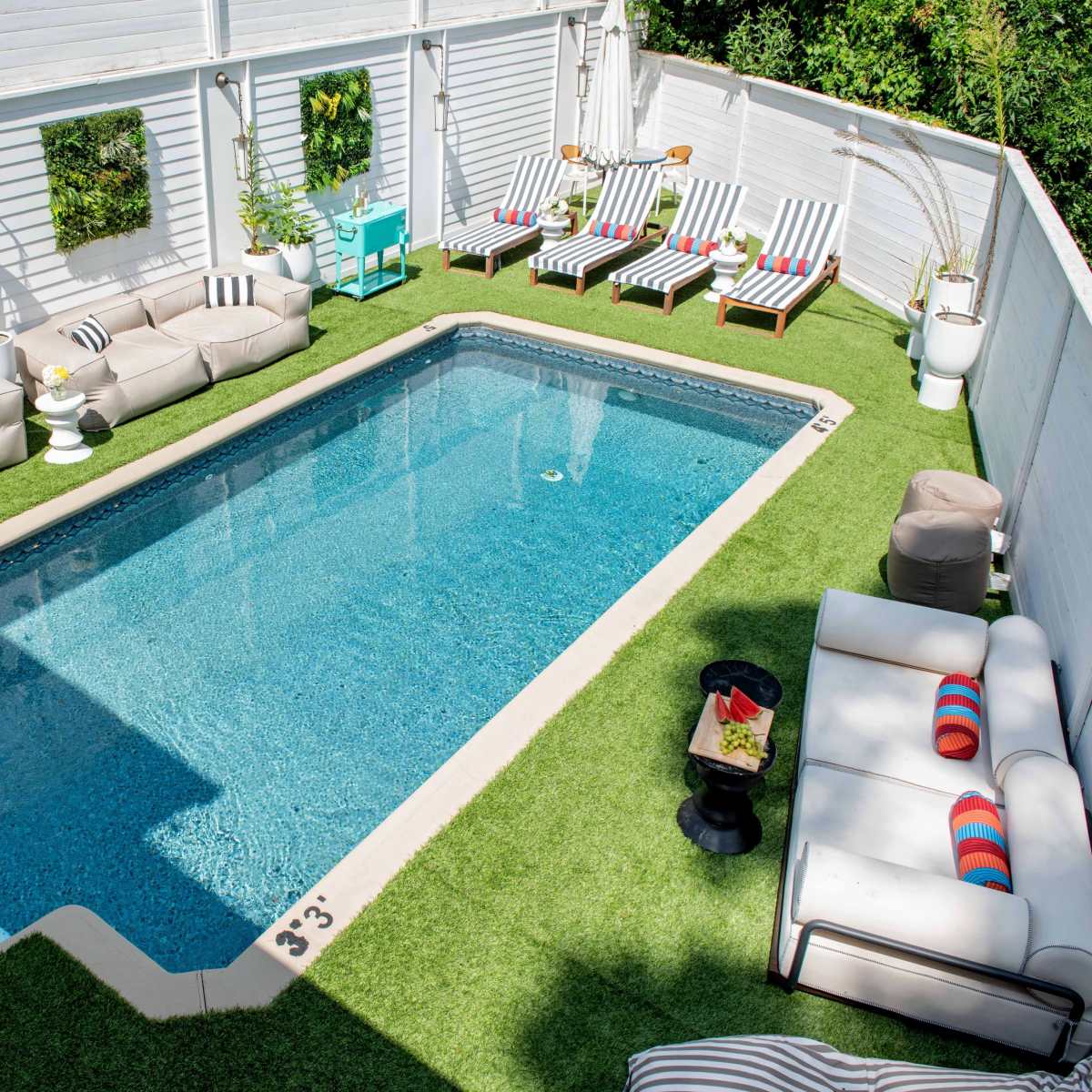 A rectangular swimming pool surrounded by green artificial grass and outdoor seating areas, including lounge chairs and sofas.