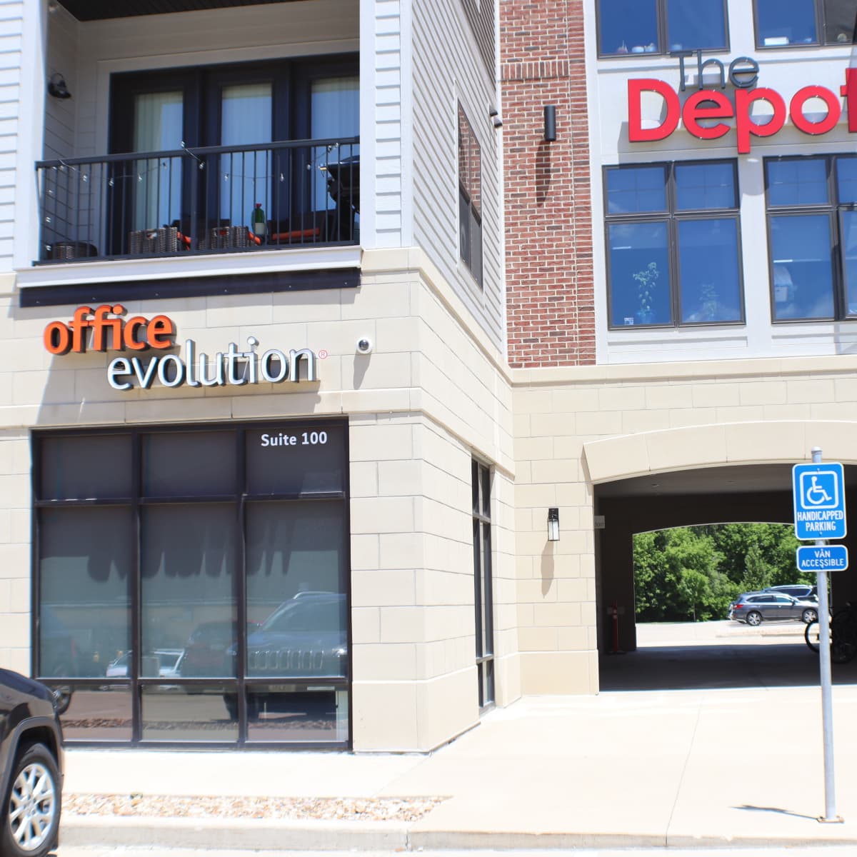 A commercial building featuring a sign for "office evolution" and another for "the Depot," along with a designated parking space for the handicapped.