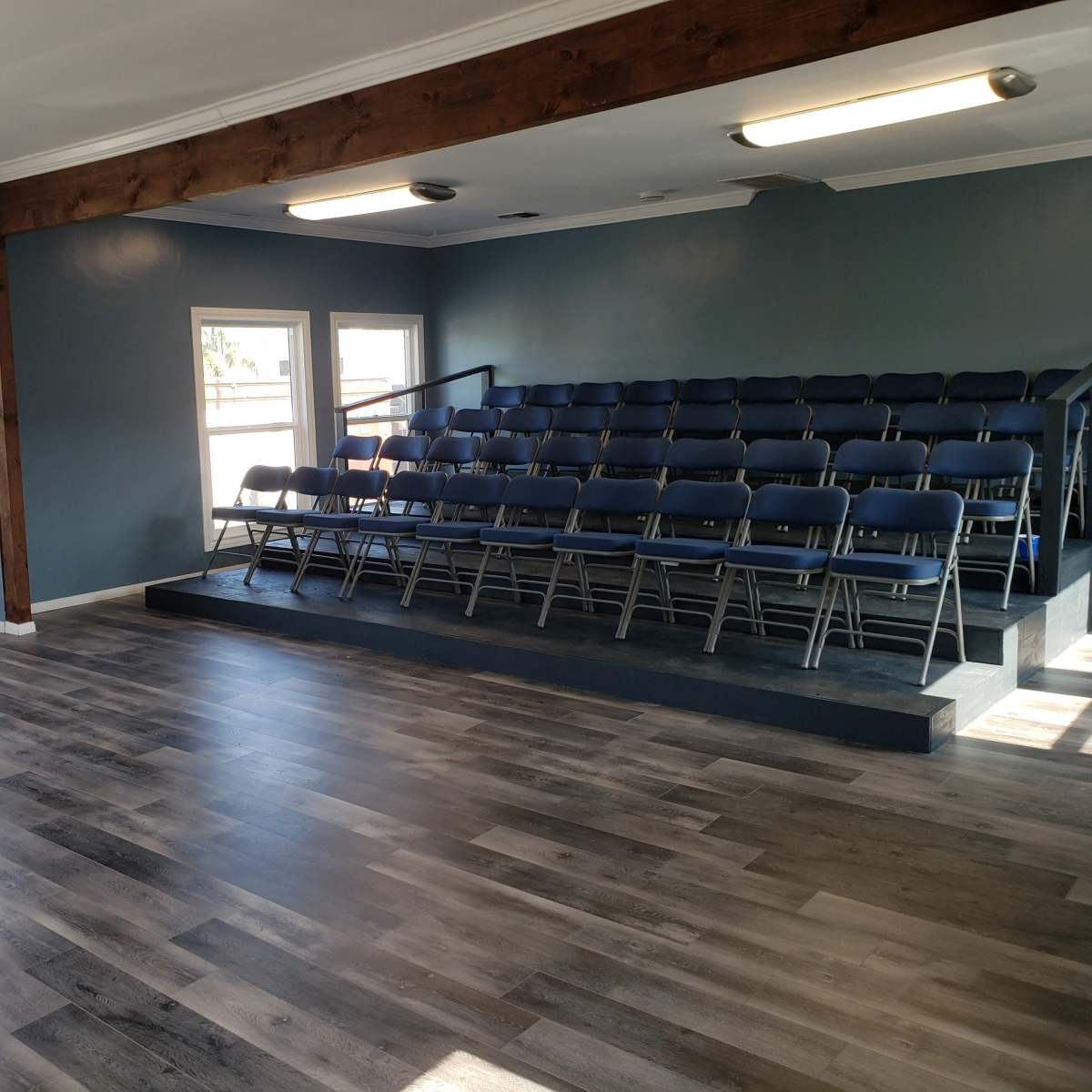 A spacious room with blue walls, a wooden beam, and rows of metal folding chairs on a raised platform.