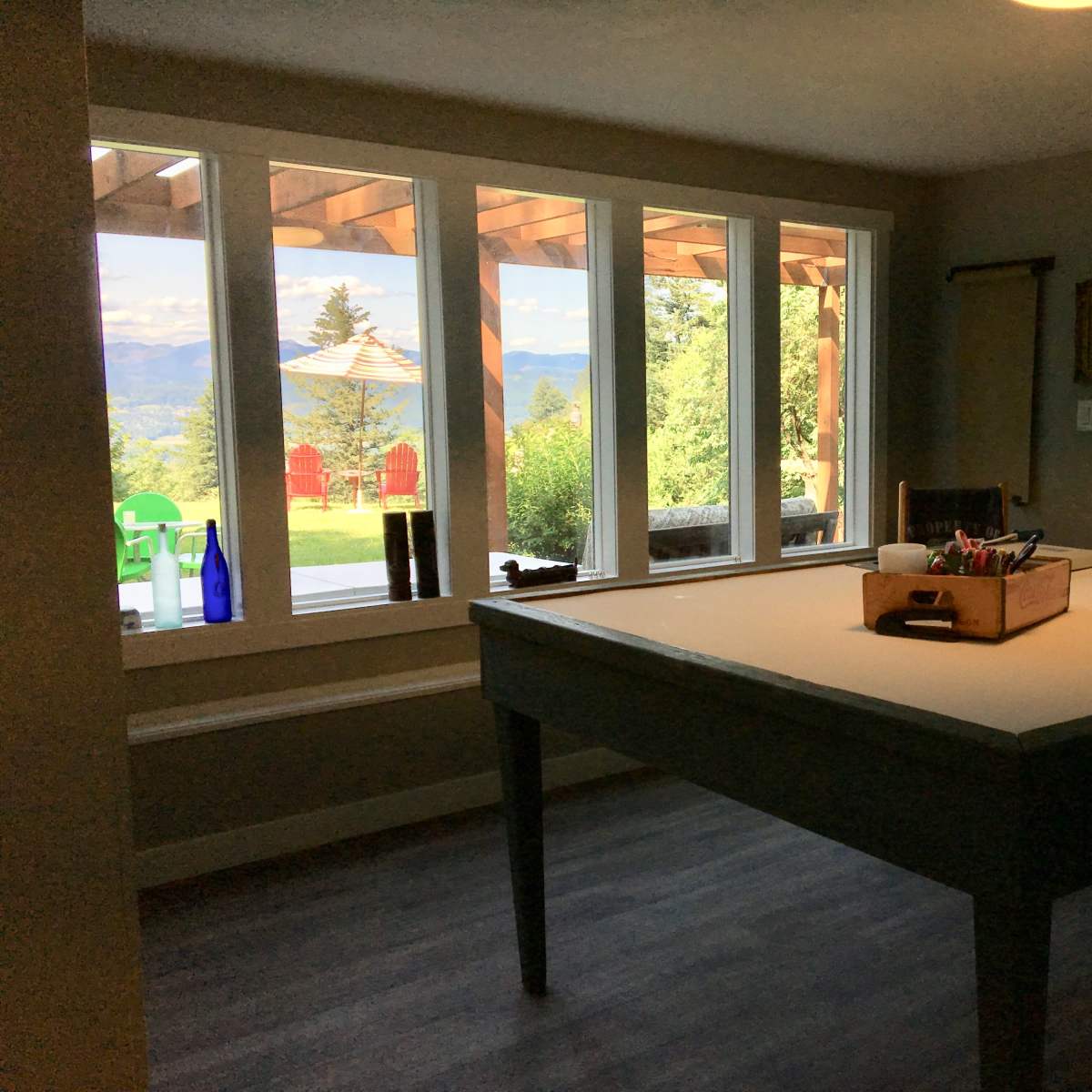 A large table with a box of supplies sits in a brightly lit room featuring large windows that overlook a scenic outdoor area.