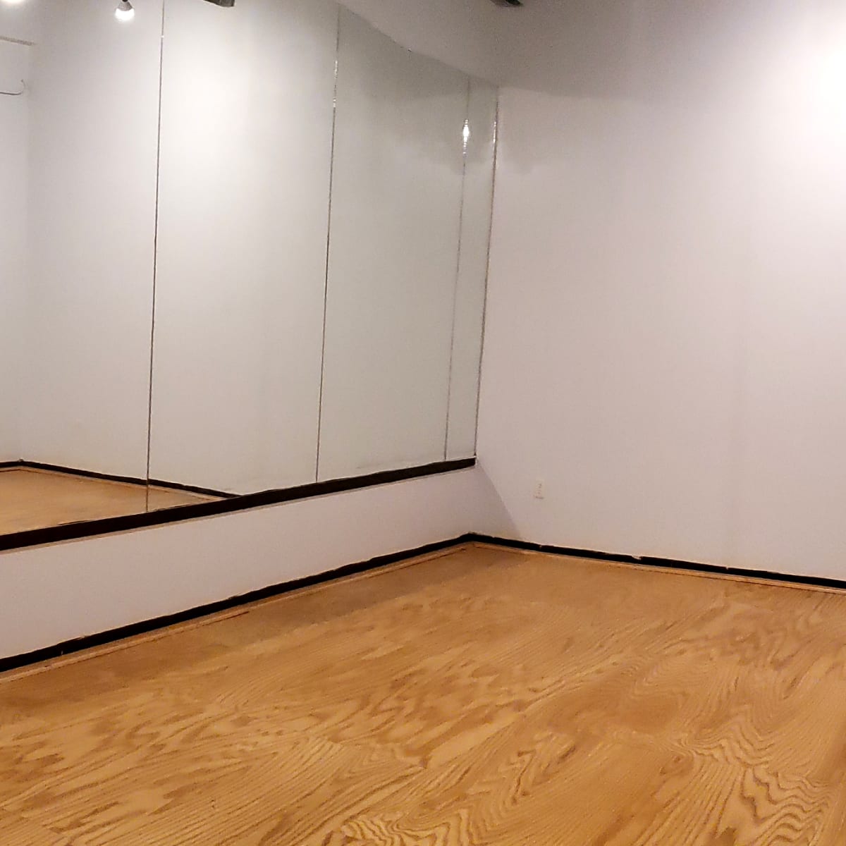 A spacious, empty room with wooden flooring and two large mirrors on one wall.