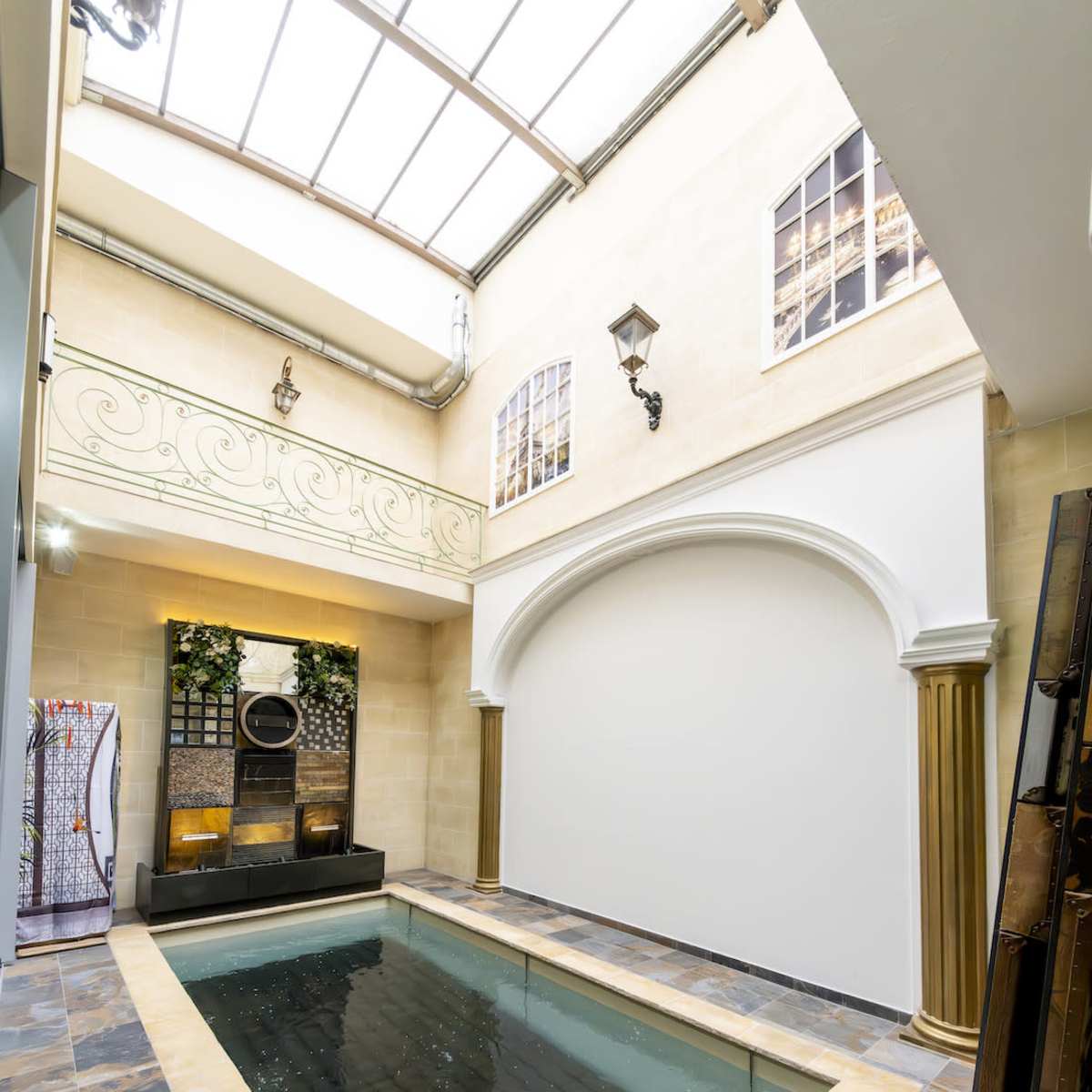 An indoor swimming pool bordered by stone walls and adorned with columns and large windows overhead.