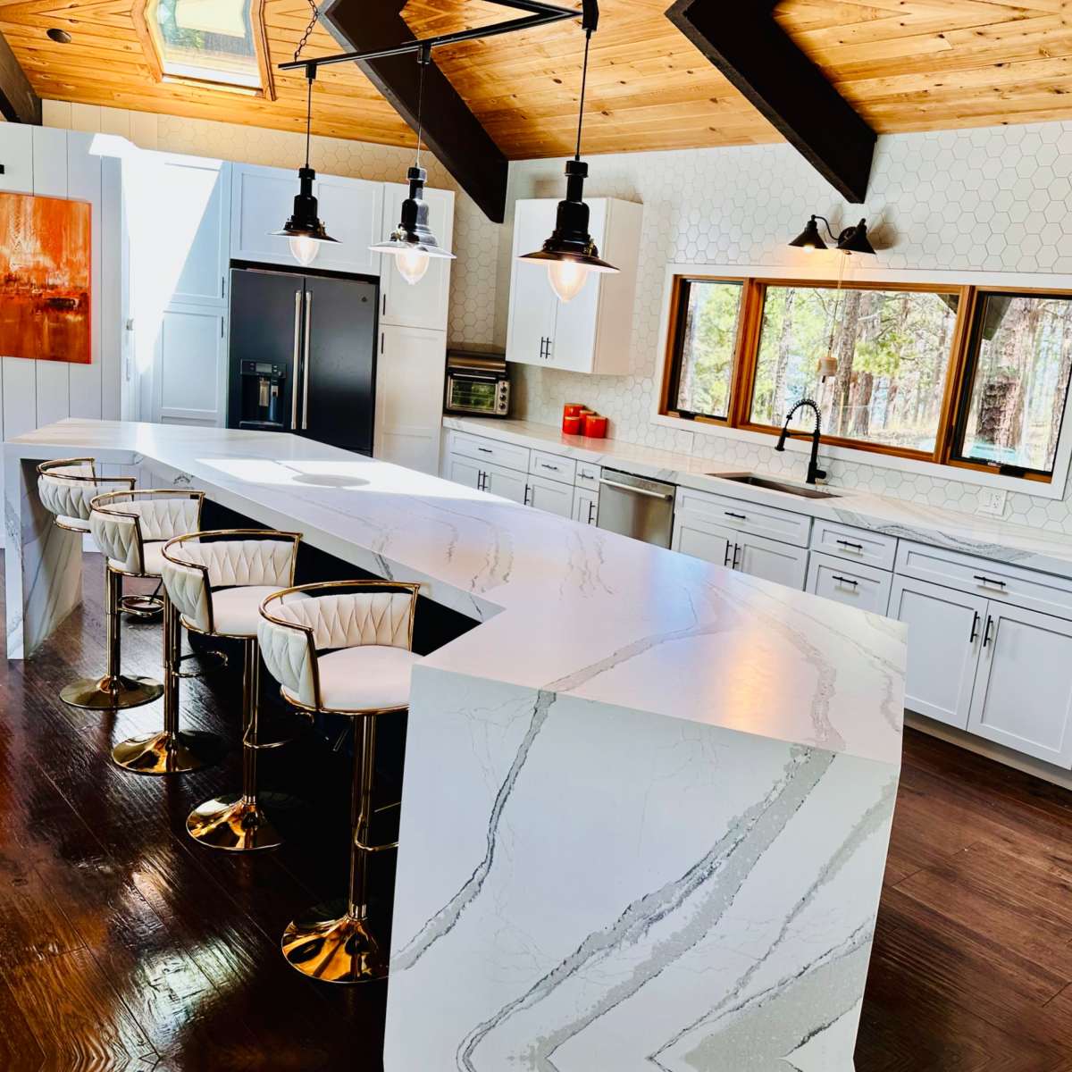 A modern kitchen features a large island with a marble countertop, sleek white cabinetry, and pendant lighting in a space with wooden beams and a hexagonal tile backsplash.