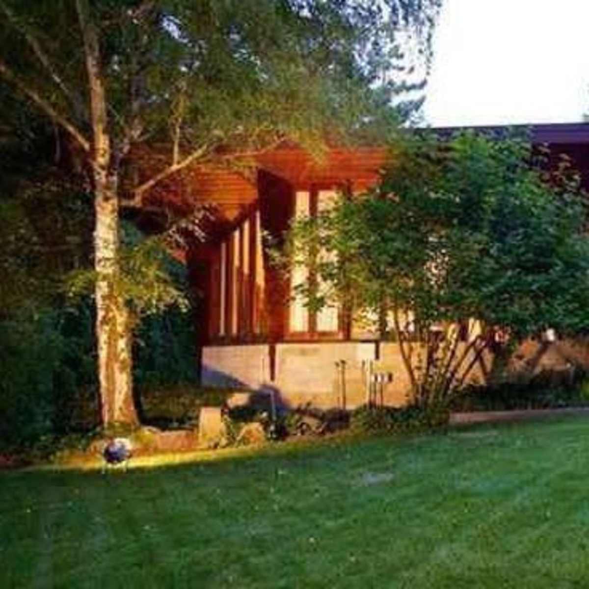 A modern home with large windows and a flat roof is situated in a landscaped yard surrounded by trees.