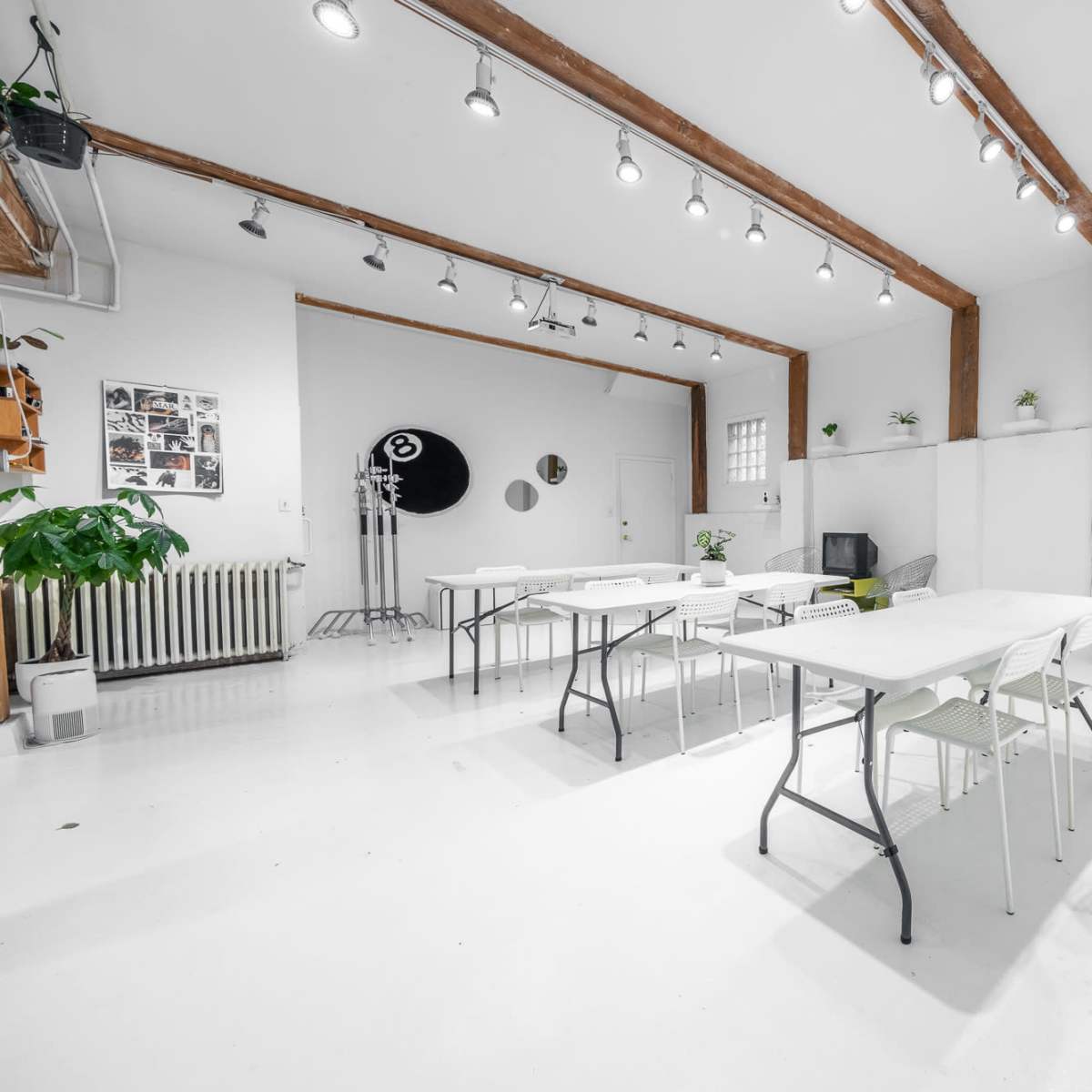 A bright, minimalist workspace with white walls, several folding tables, and overhead lighting.