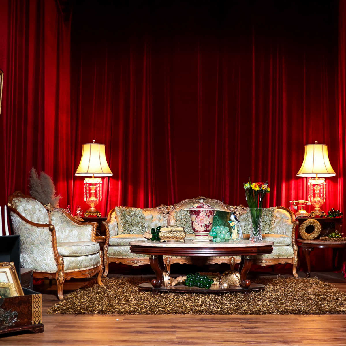 The scene features a vintage-style living room with a red curtain backdrop, decorated with ornate furniture, lamps, a central table, and various pieces of luggage.