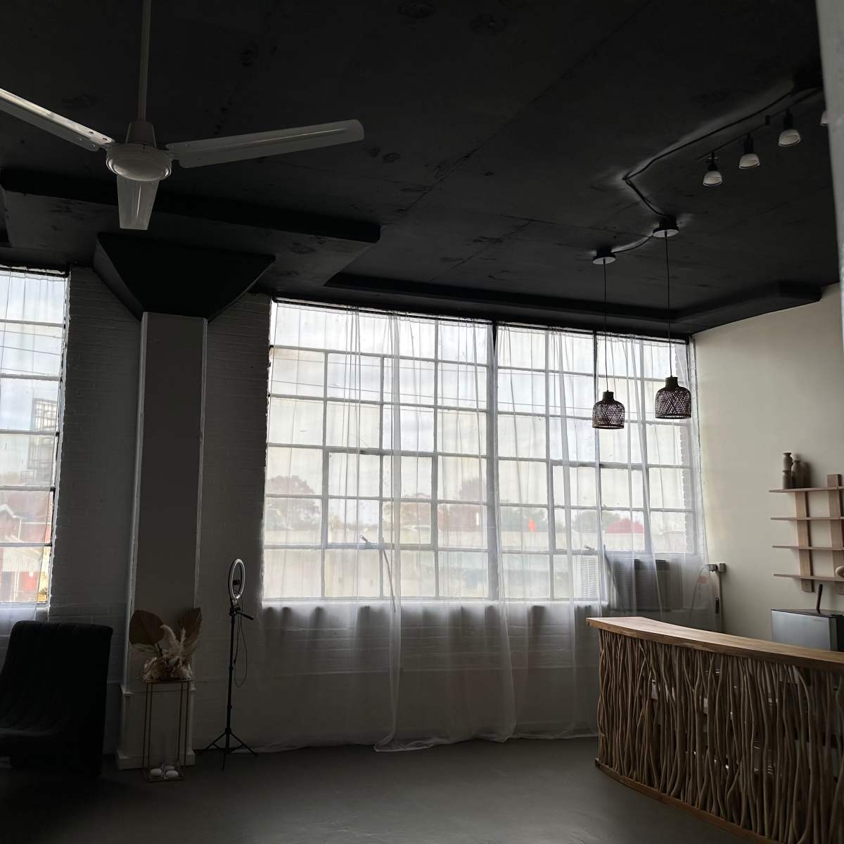 A spacious room with large windows covered by sheer curtains, a ceiling fan, and a curved seating area, along with a reception desk and decorative elements on the walls.