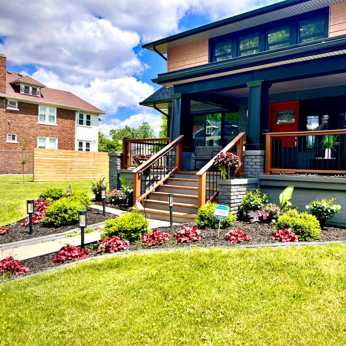 A well-maintained house with a front porch, stairs leading up to it, and landscaped gardens featuring various plants and flowers.