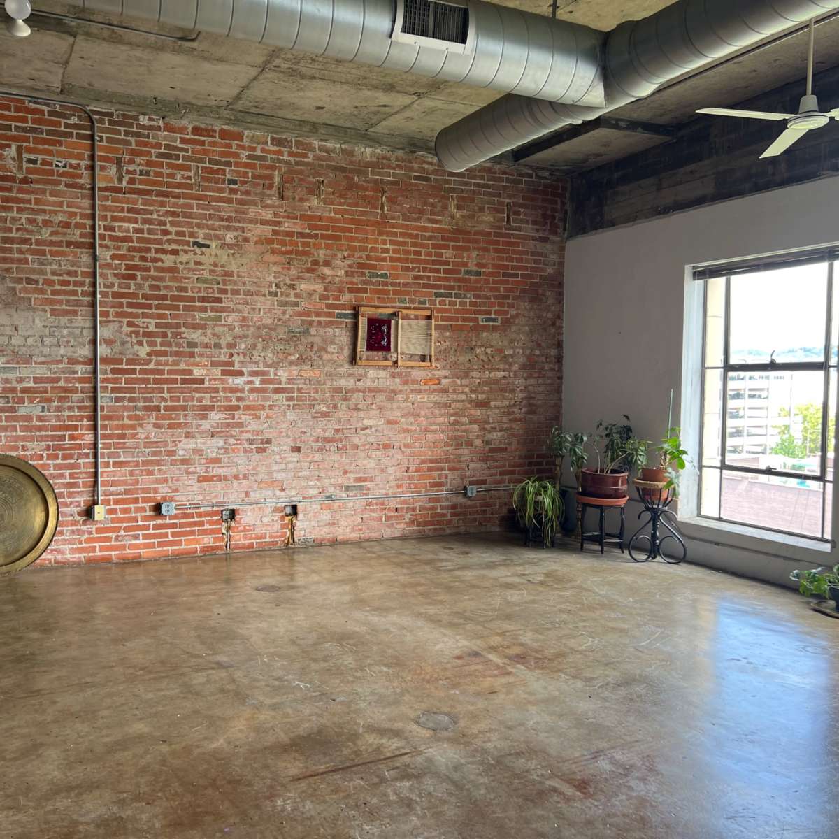 An industrial-style room featuring a brick wall, concrete flooring, and large windows with potted plants nearby.