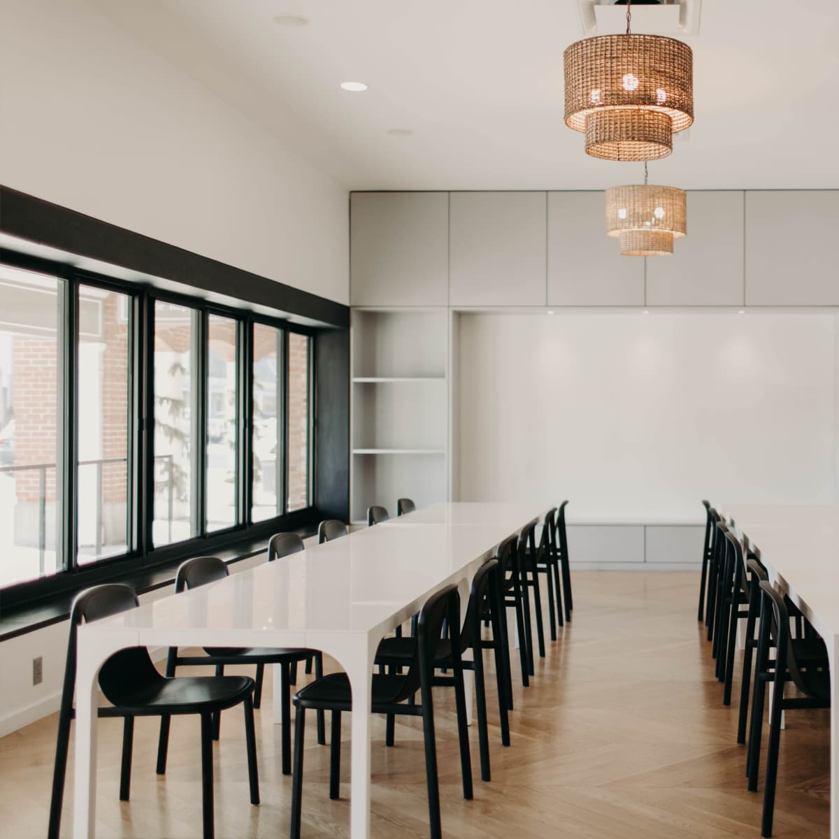 A modern conference room features a long white table surrounded by black chairs, illuminated by stylish pendant lights.
