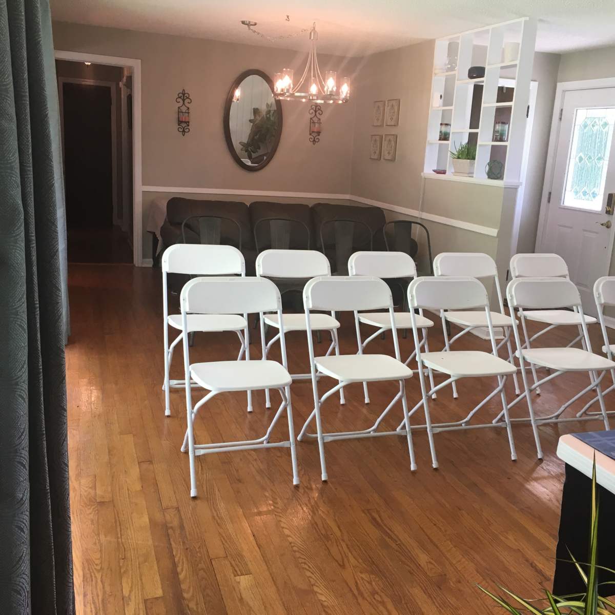 A room with wooden floors, featuring a set of white folding chairs arranged in rows and a small table in the foreground.