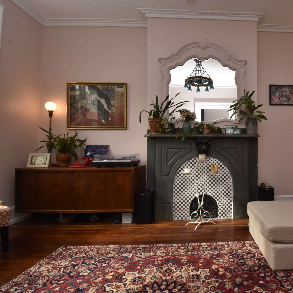 A cozy living room with a light pink wall, a fireplace centered in the back, and a sectional sofa on the right.