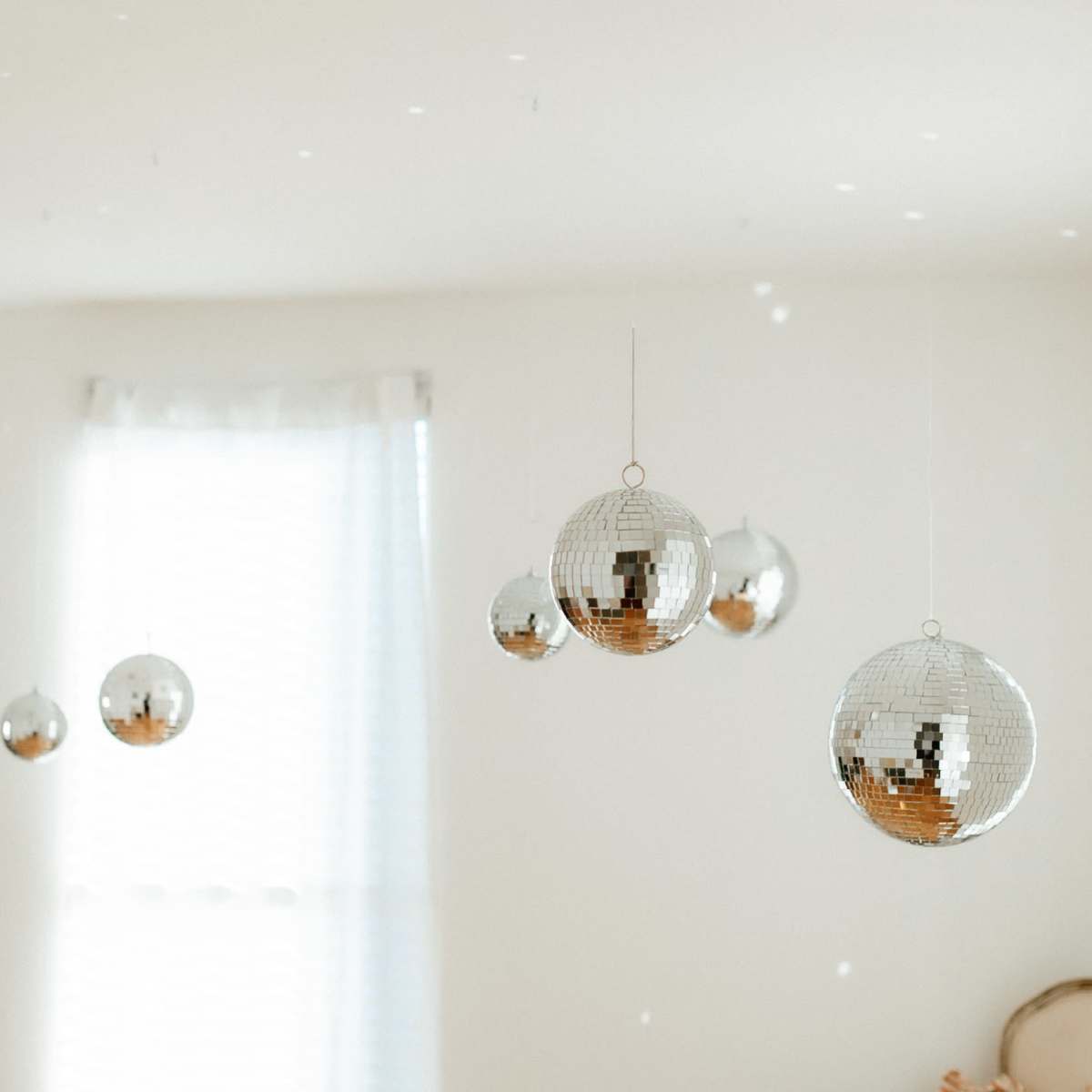 Several hanging disco balls reflecting light in a room with white walls and a window.
