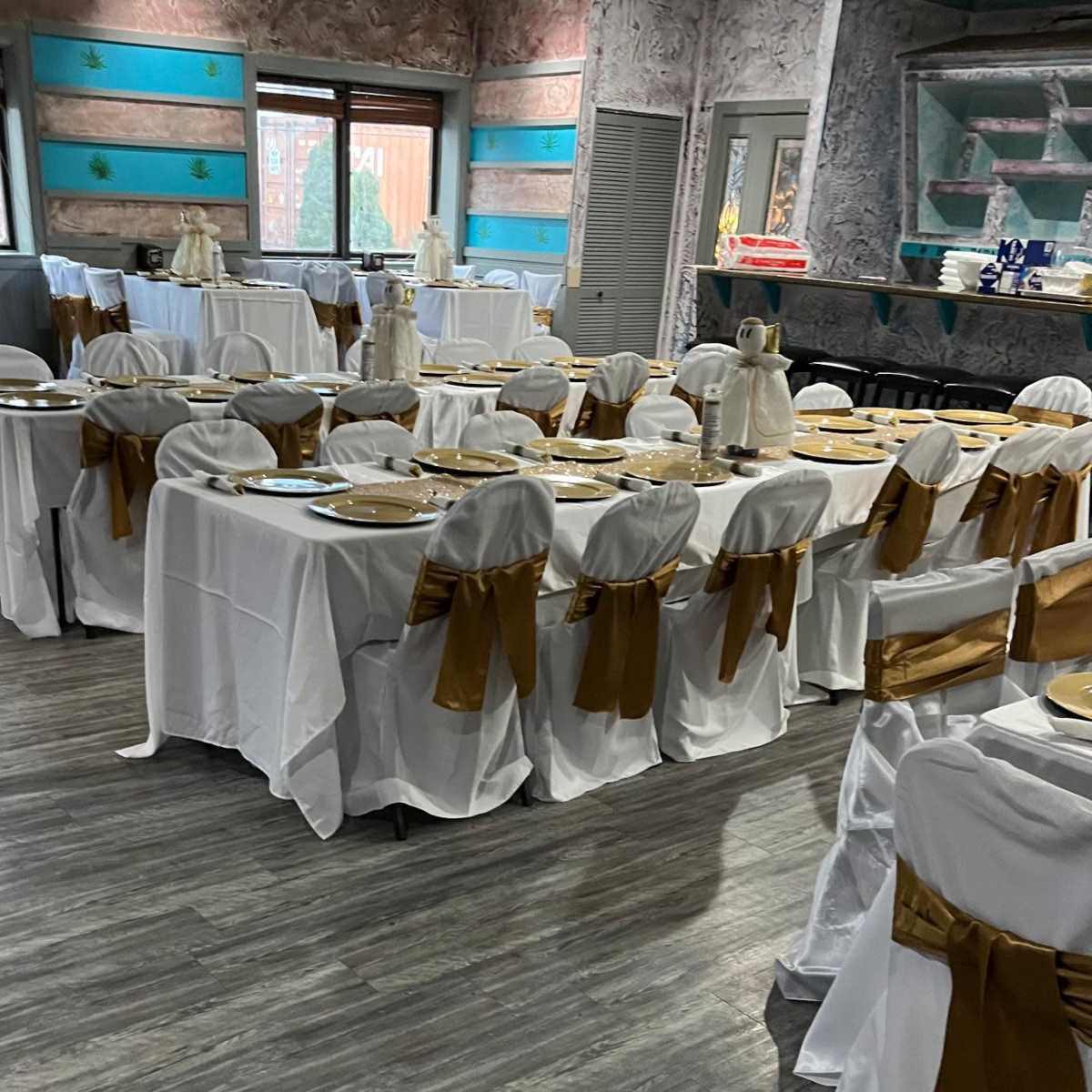 A banquet hall set up with multiple tables covered in white tablecloths and adorned with gold chair sashes.