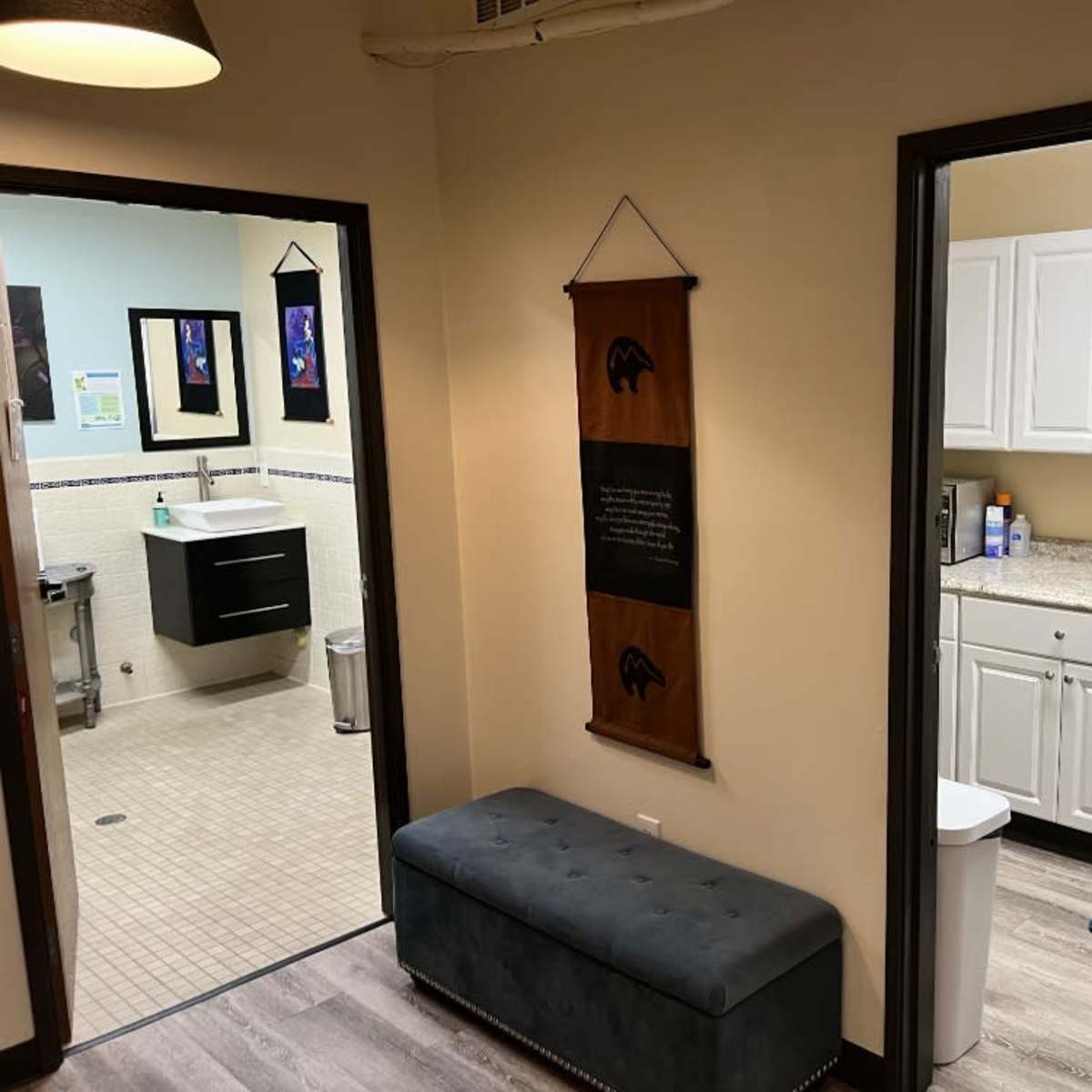 A hallway leading to two rooms; one on the left is a bathroom with a sink and toilet, and the one on the right is a kitchen area with cabinets and a countertop.