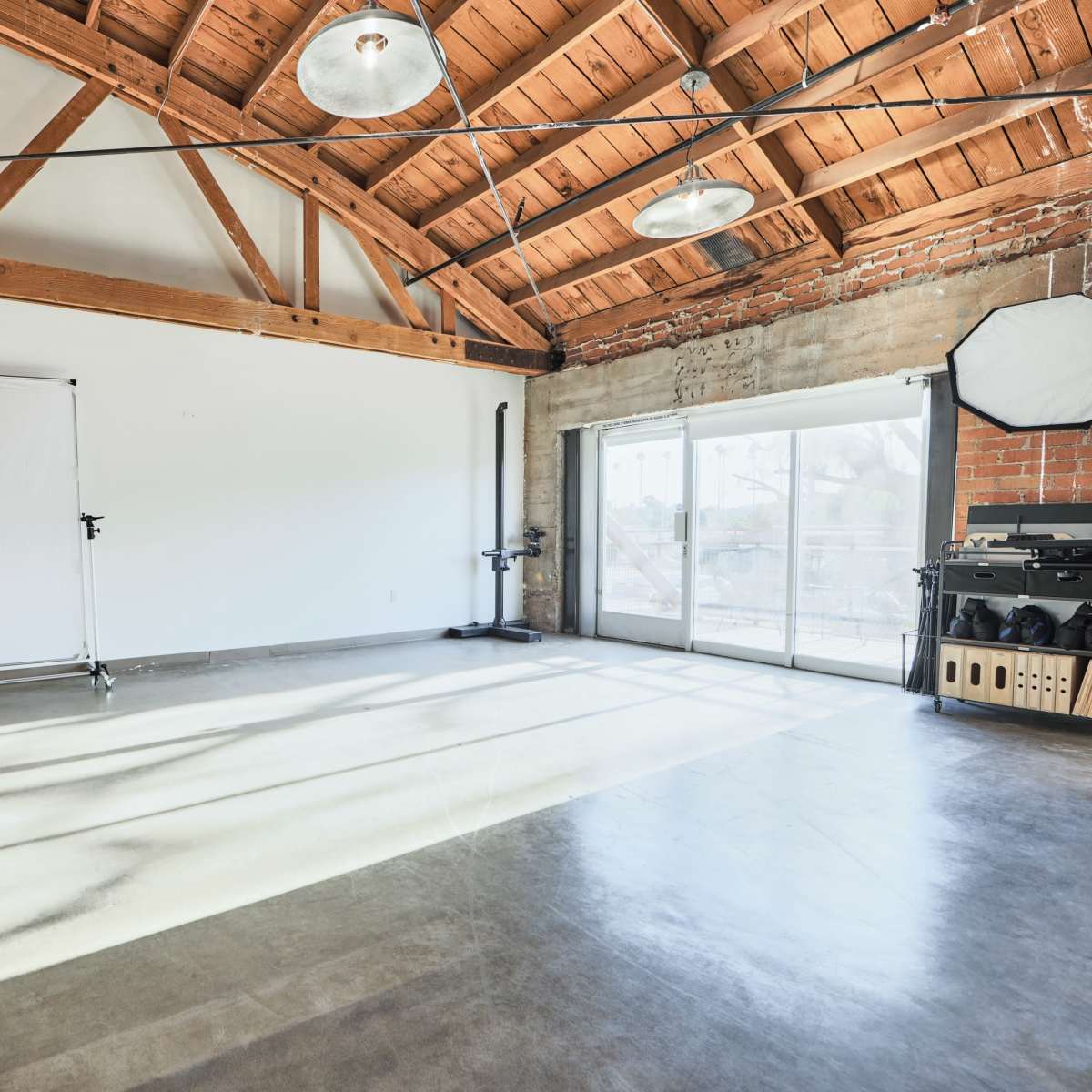 A spacious, industrial-style interior with exposed wooden beams, concrete flooring, and large windows letting in natural light.