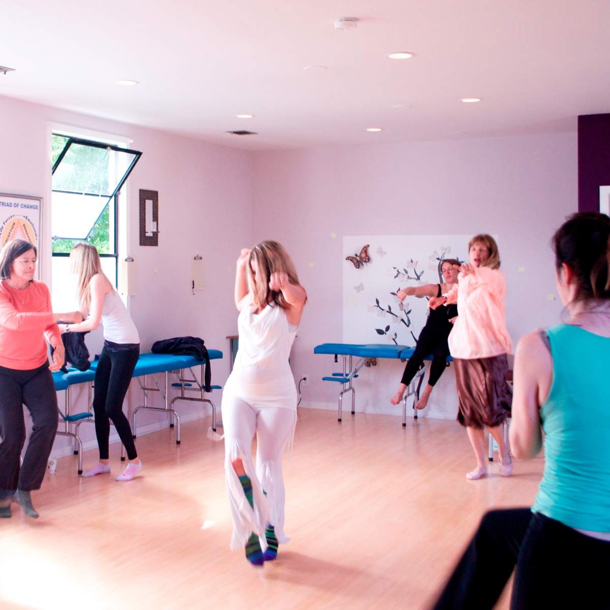 A group of people is engaged in a dance movement activity in a brightly lit studio.