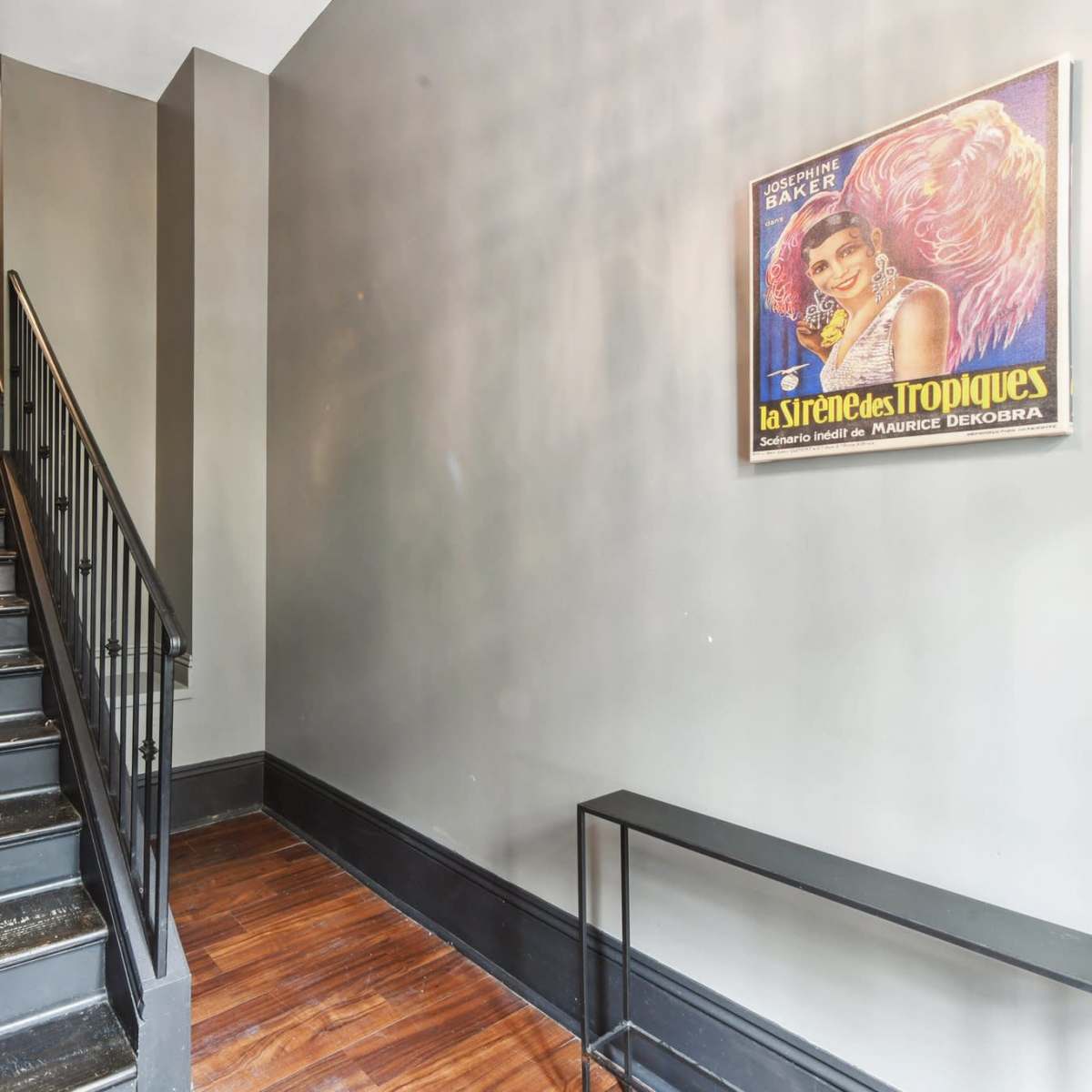 A staircase with black steps leading upward, paired with a framed vintage poster on the wall beside it.