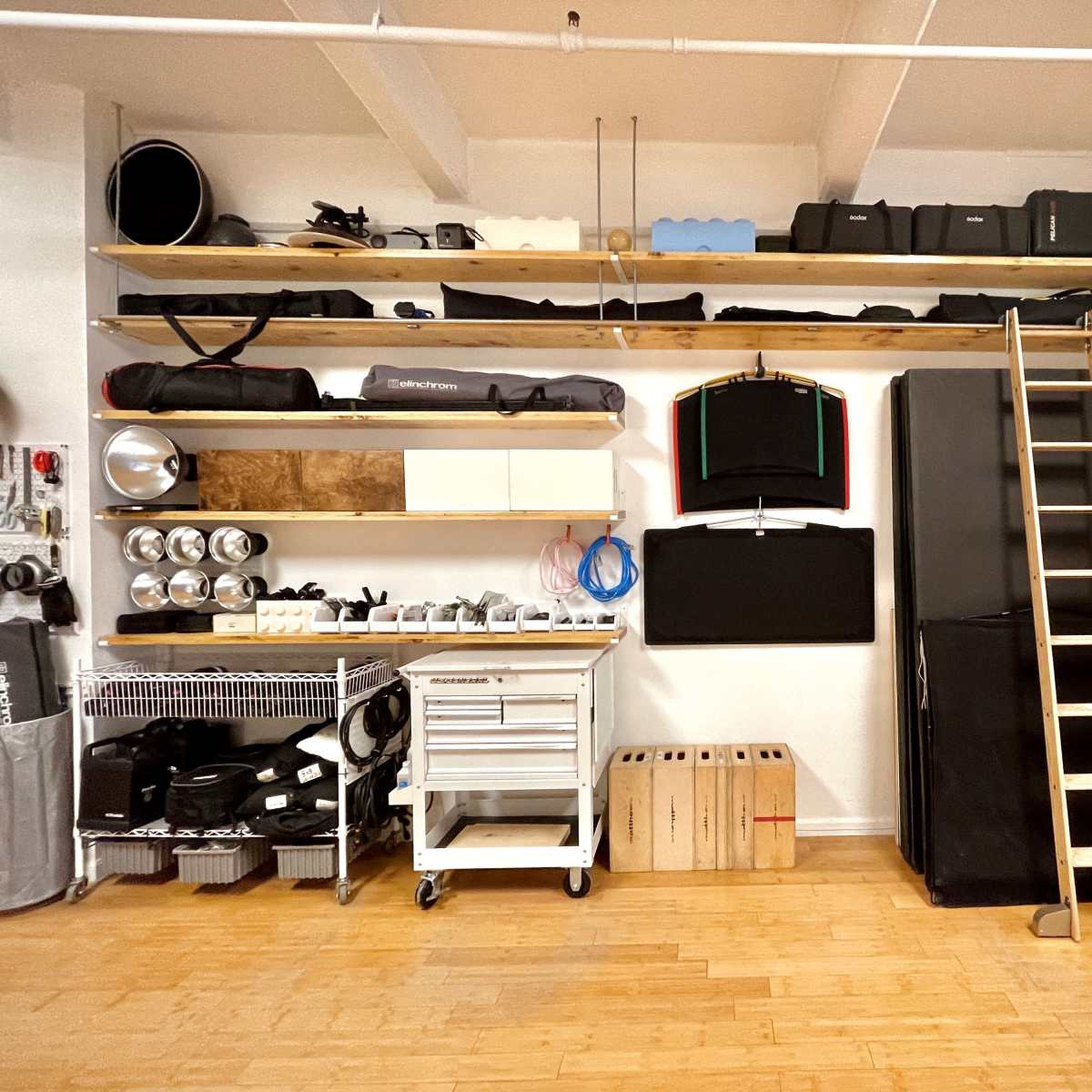 A neatly organized storage space with shelves holding various equipment, a ladder leaning against the wall, and a cart with tools.