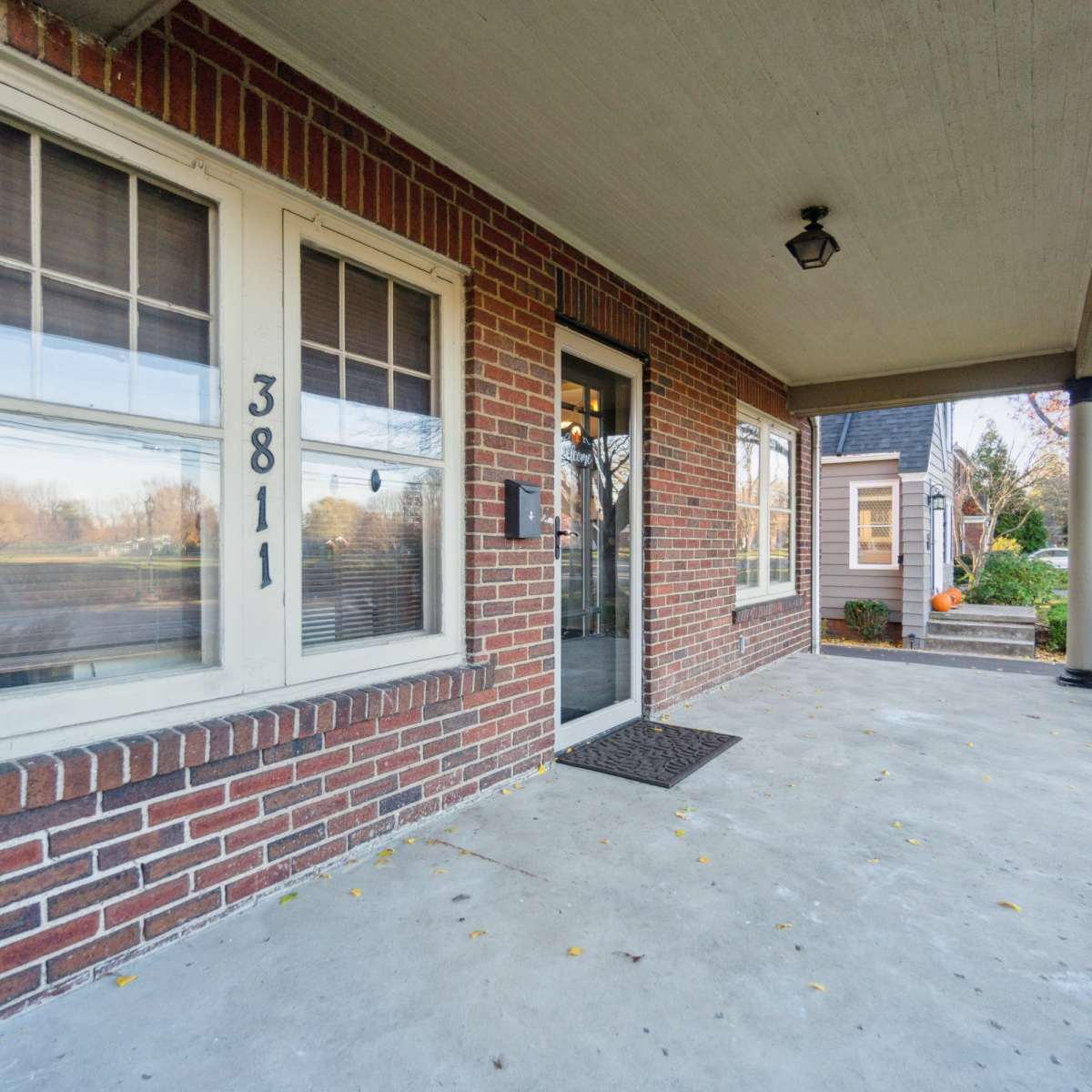 A brick porch entrance with a glass door and large windows, featuring a house number displayed prominently.