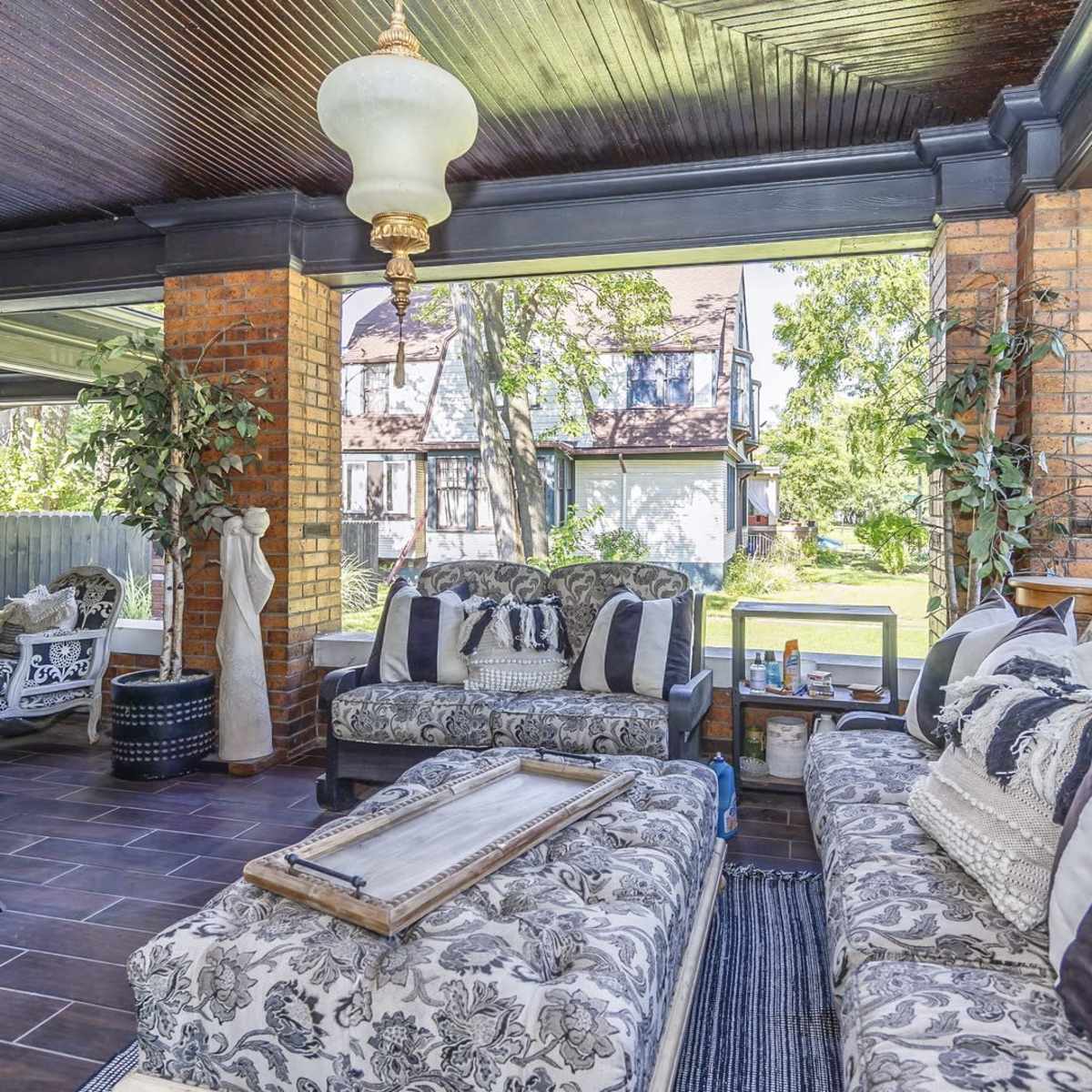 A covered outdoor living area with floral-patterned furniture, a coffee table, and large windows overlooking a garden.