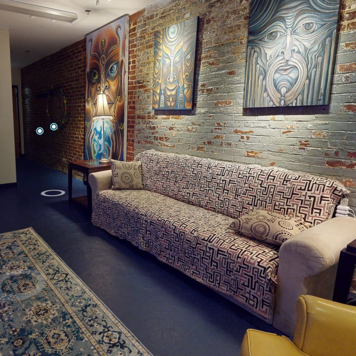 A neatly arranged room with a patterned sofa, framed artwork on the brick walls, and a decorative rug on the floor.