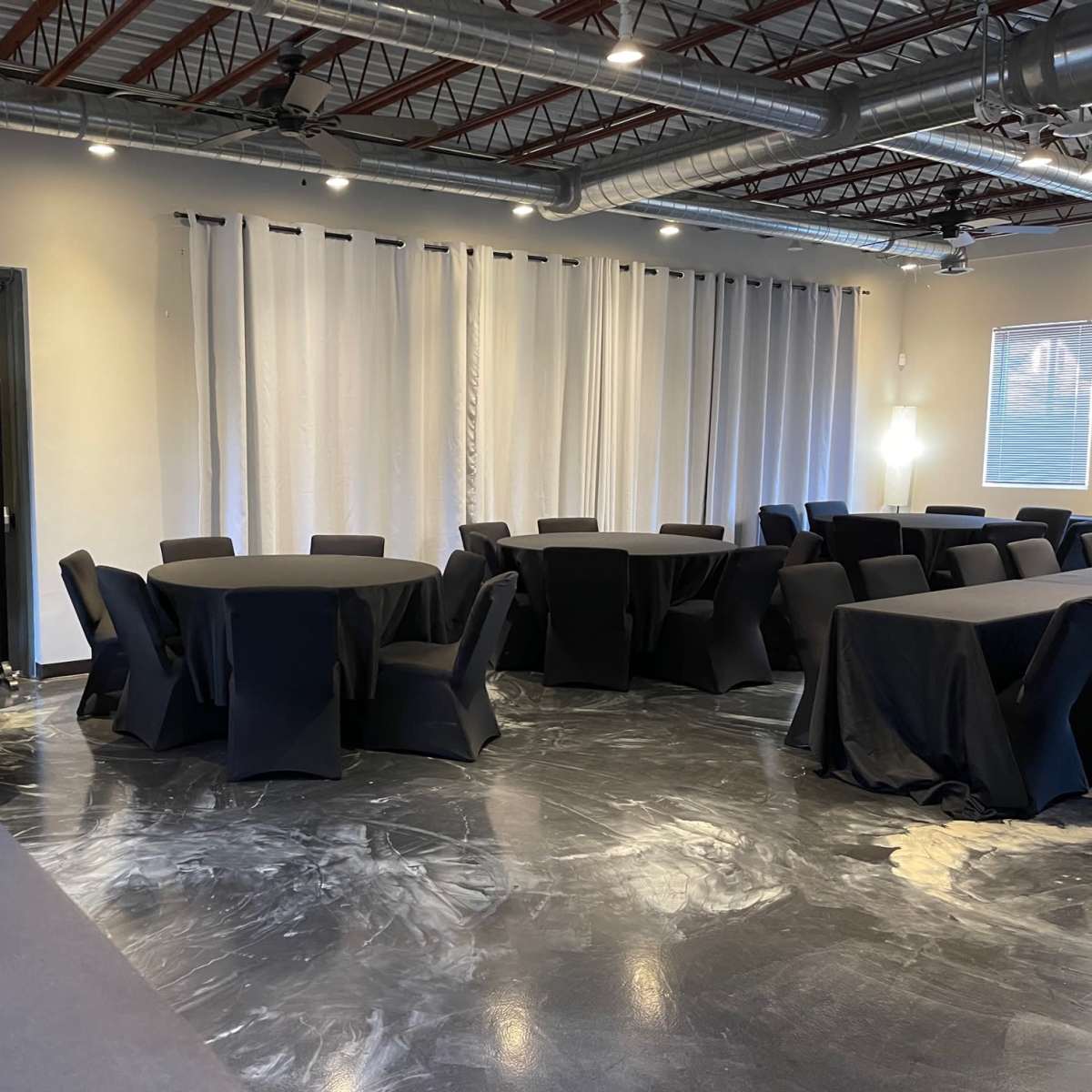 An event space with several black round tables and chairs arranged neatly in a well-lit area.