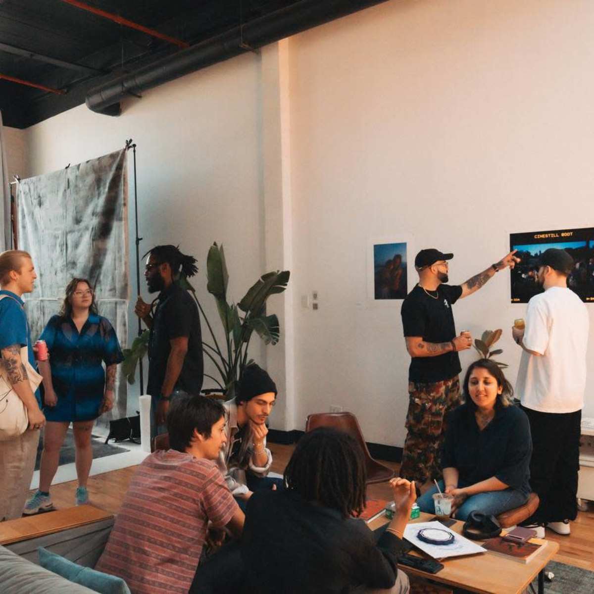 A group of people interacts in a spacious, well-lit room filled with plants and clothing displays.