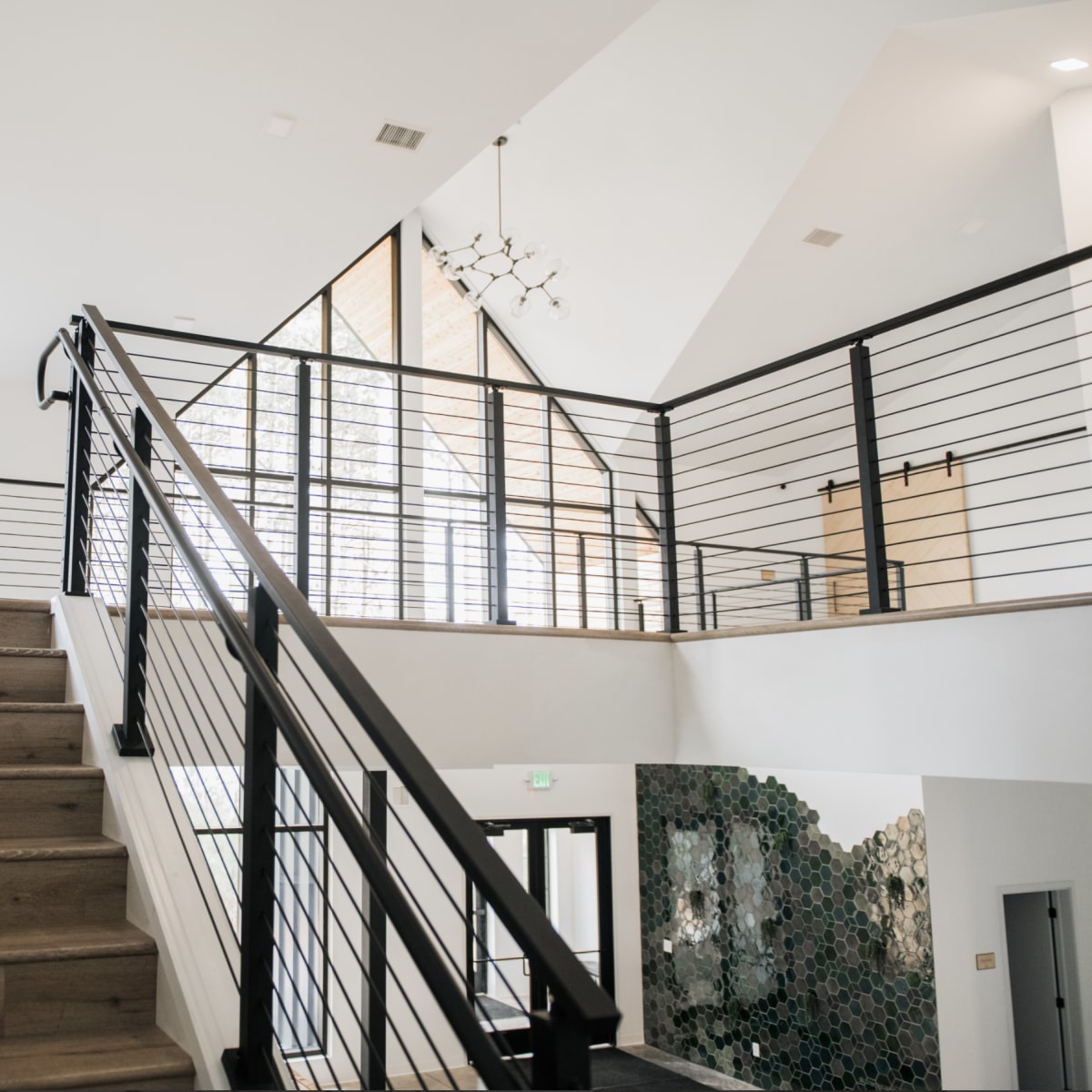 A modern interior staircase with wooden steps leading to a second level, featuring a railing and a large window that allows natural light to enter the space.