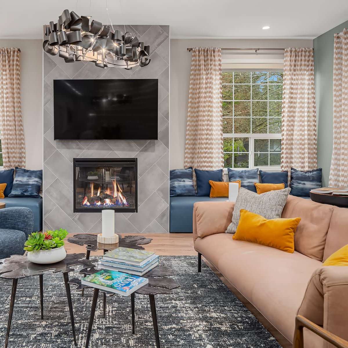 The living room features a fireplace set against a tiled wall, with a large television above it, surrounded by seating that includes a beige sofa and blue chairs.