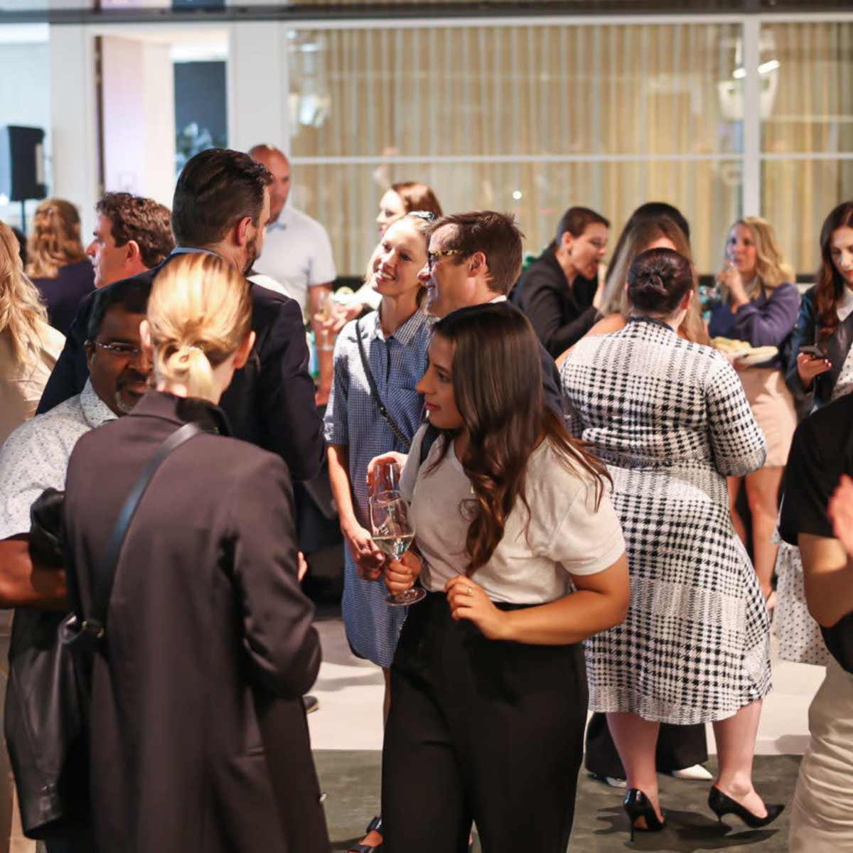 A large group of people socialize at a networking event in a modern indoor space.