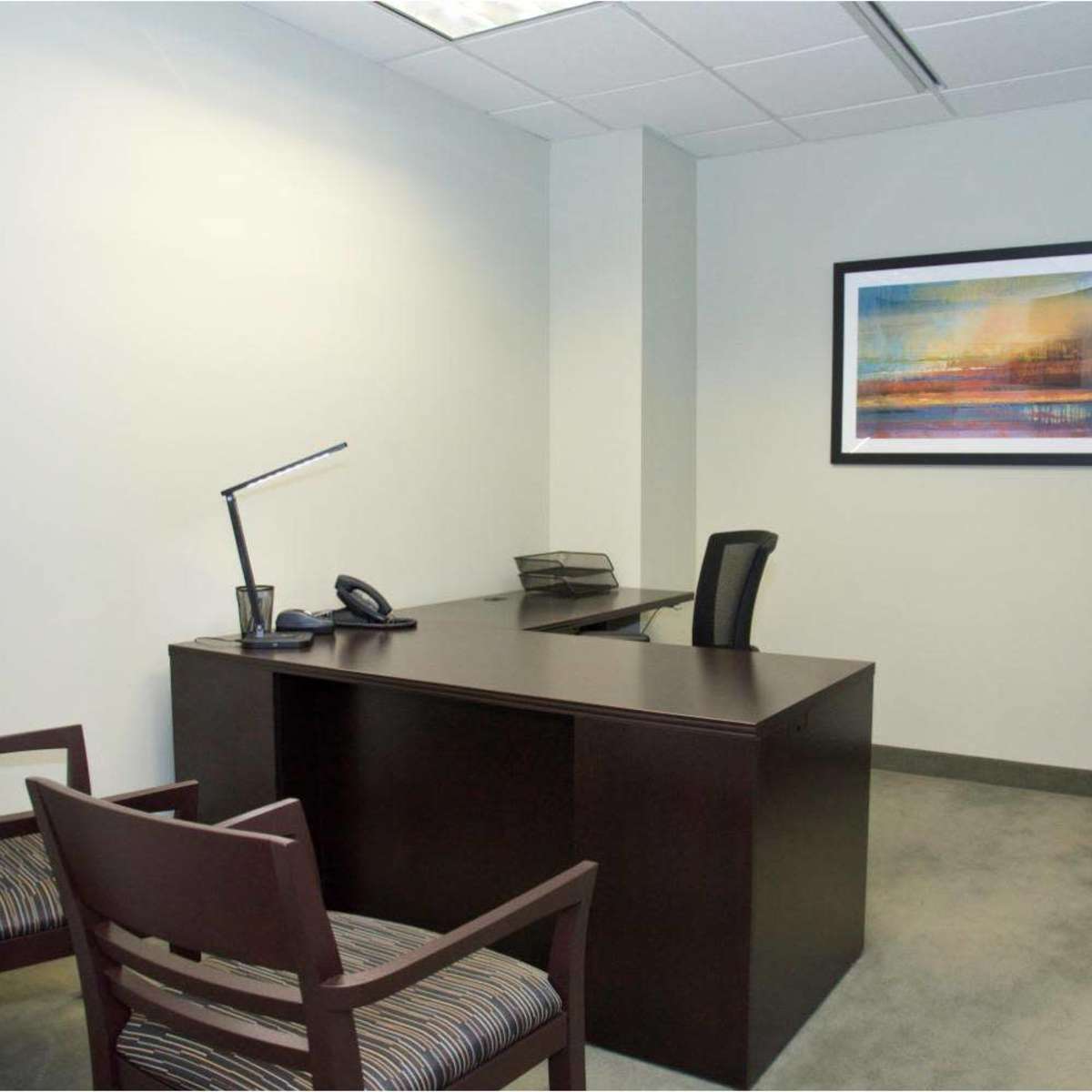 A minimalistic office space featuring a desk, an office chair, two visitor chairs, a phone, and a wall-mounted artwork.