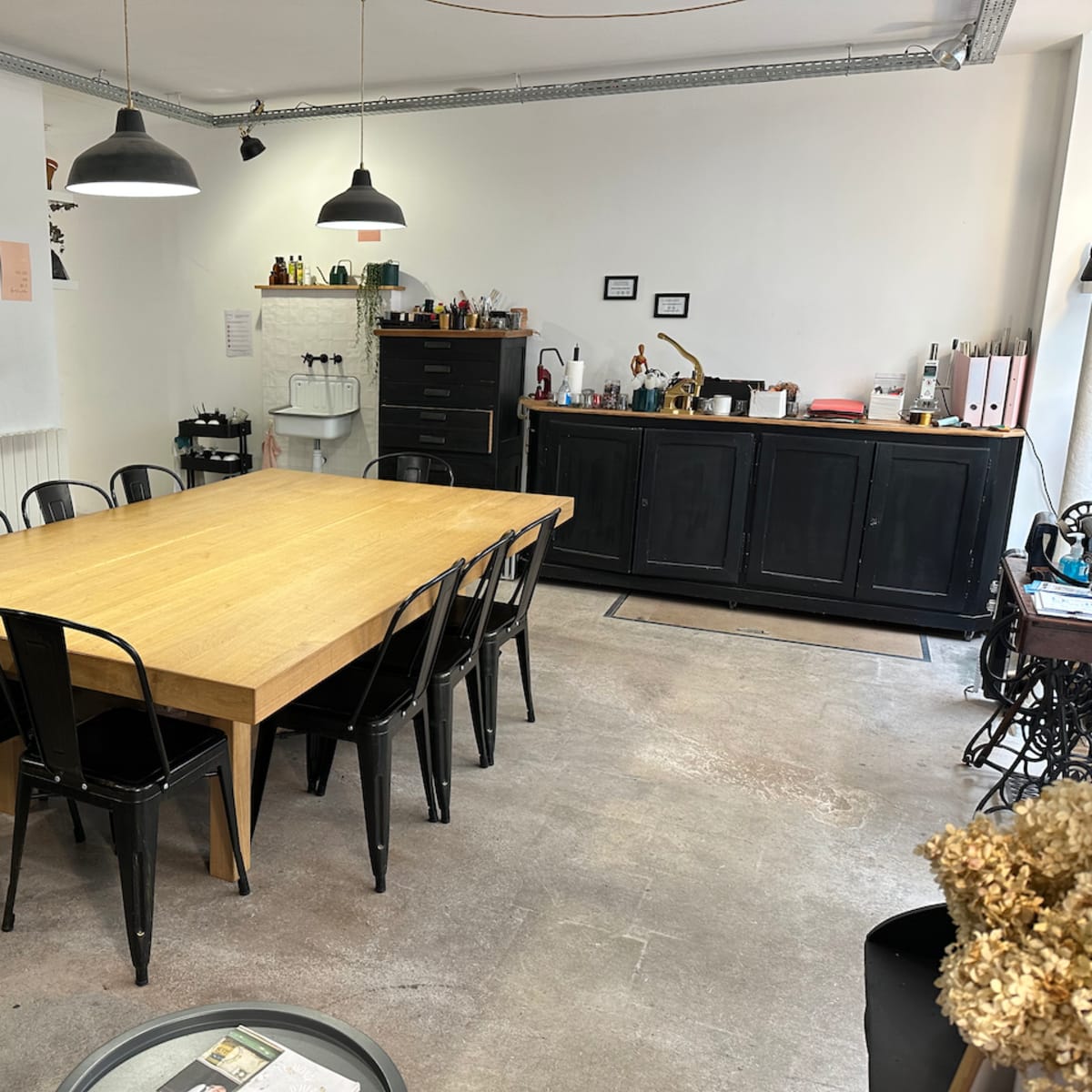 A spacious room features a large wooden table surrounded by black metal chairs, with shelves and cabinets against the walls.