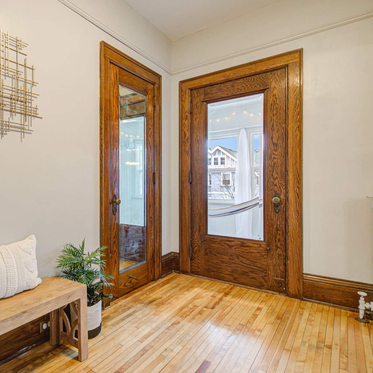 A wooden bench against a wall with a decorative artwork, leading to double doors that open to an exterior view.
