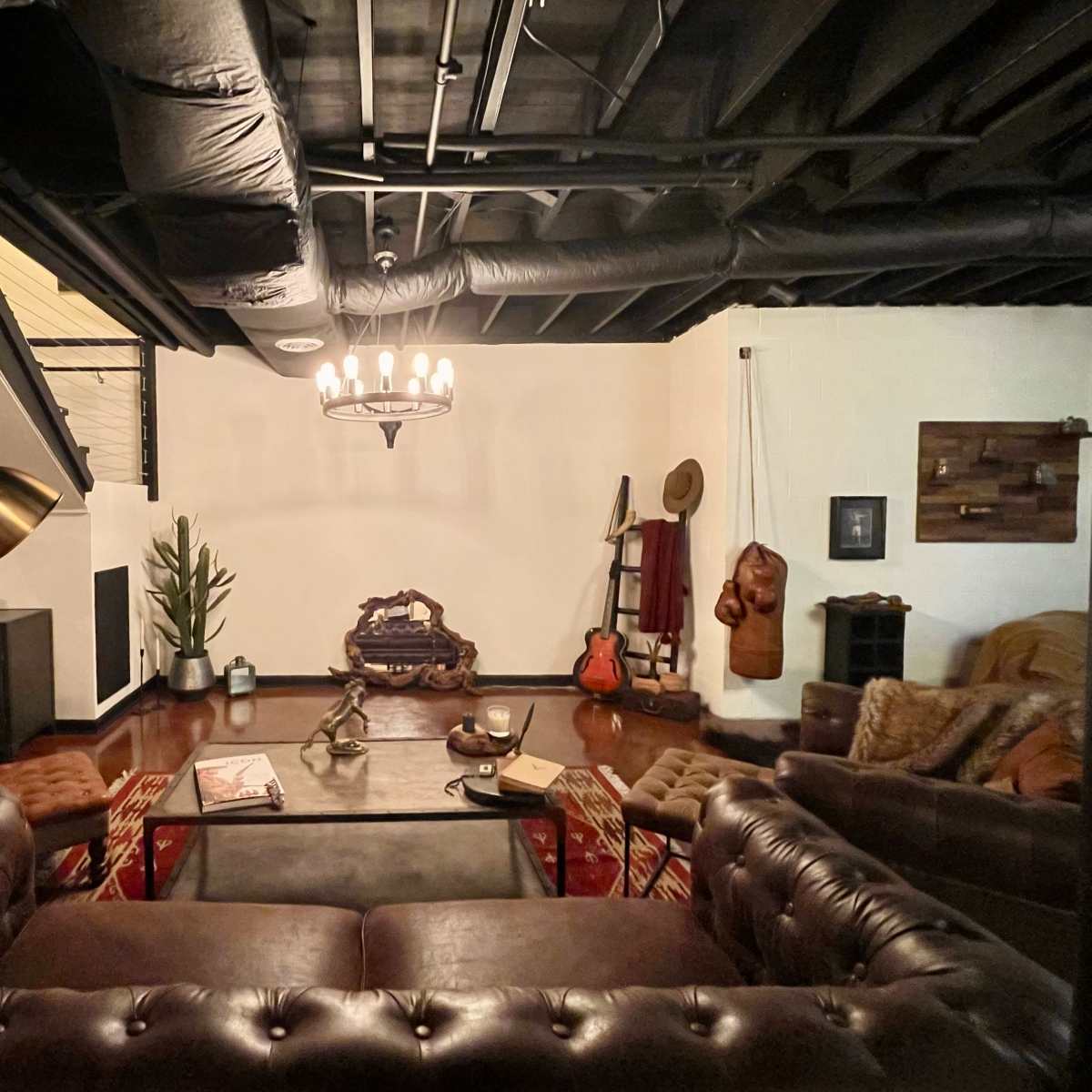 A stylish living room featuring a leather sofa set, a coffee table, a staircase, and various decorative elements including a guitar and a potted plant.