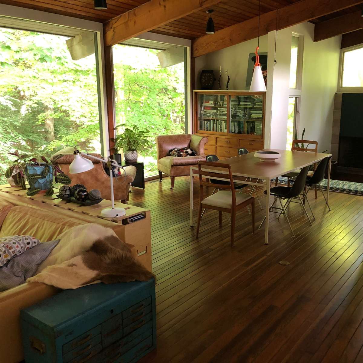 A bright, modern living space with wooden beams, a dining table, and large windows overlooking greenery.