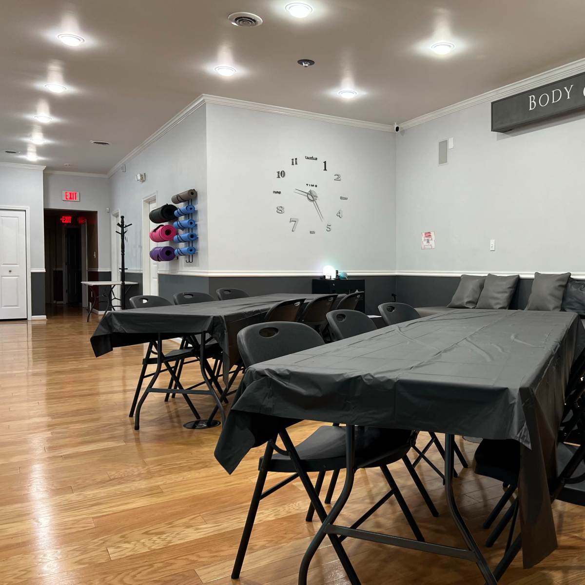 A room set up with several black folding tables and chairs, with a couch against the wall and yoga mats on a rack.