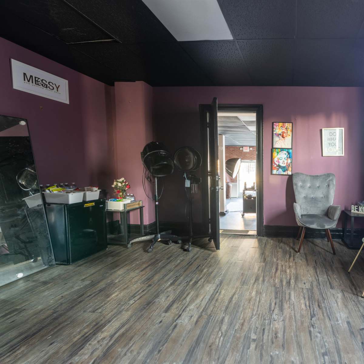 A room with purple walls, a mirror, a couple of chairs, and a doorway leading to another space.