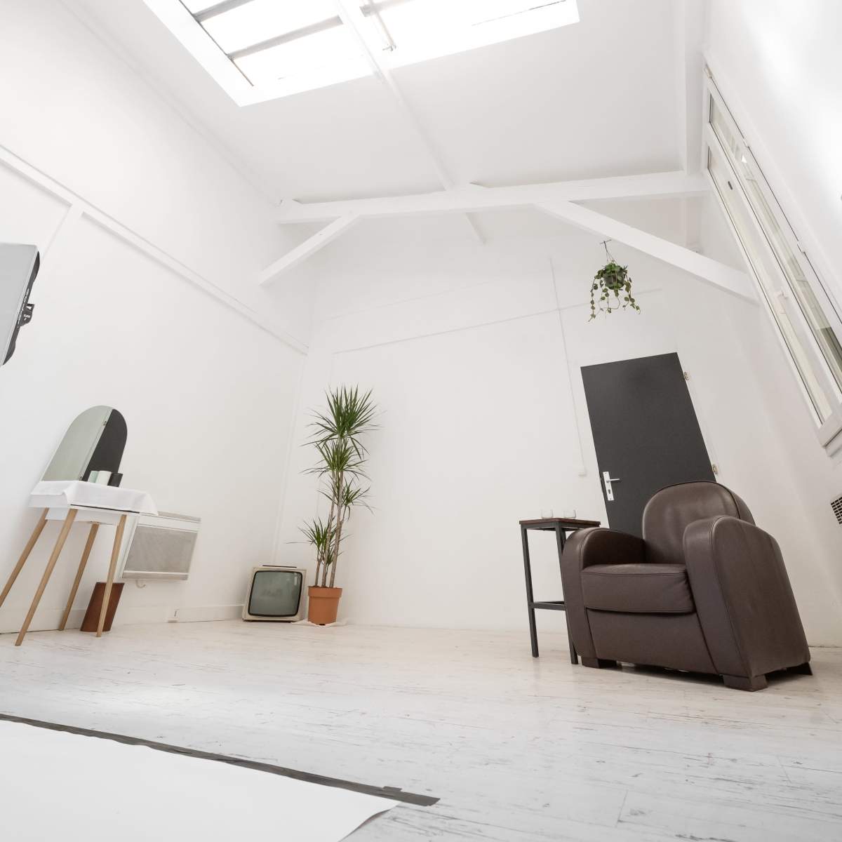 A spacious, minimalist room with a skylight, a brown leather armchair, a small table, a potted plant, and an old television set.