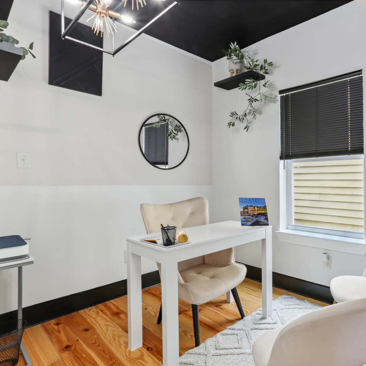 A small office space with a white table, two chairs, a circular mirror on the wall, and decorative plants.