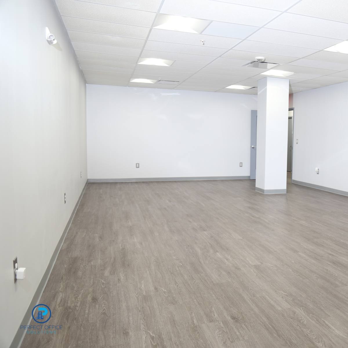 An empty, unadorned room with light-colored flooring and plain walls.