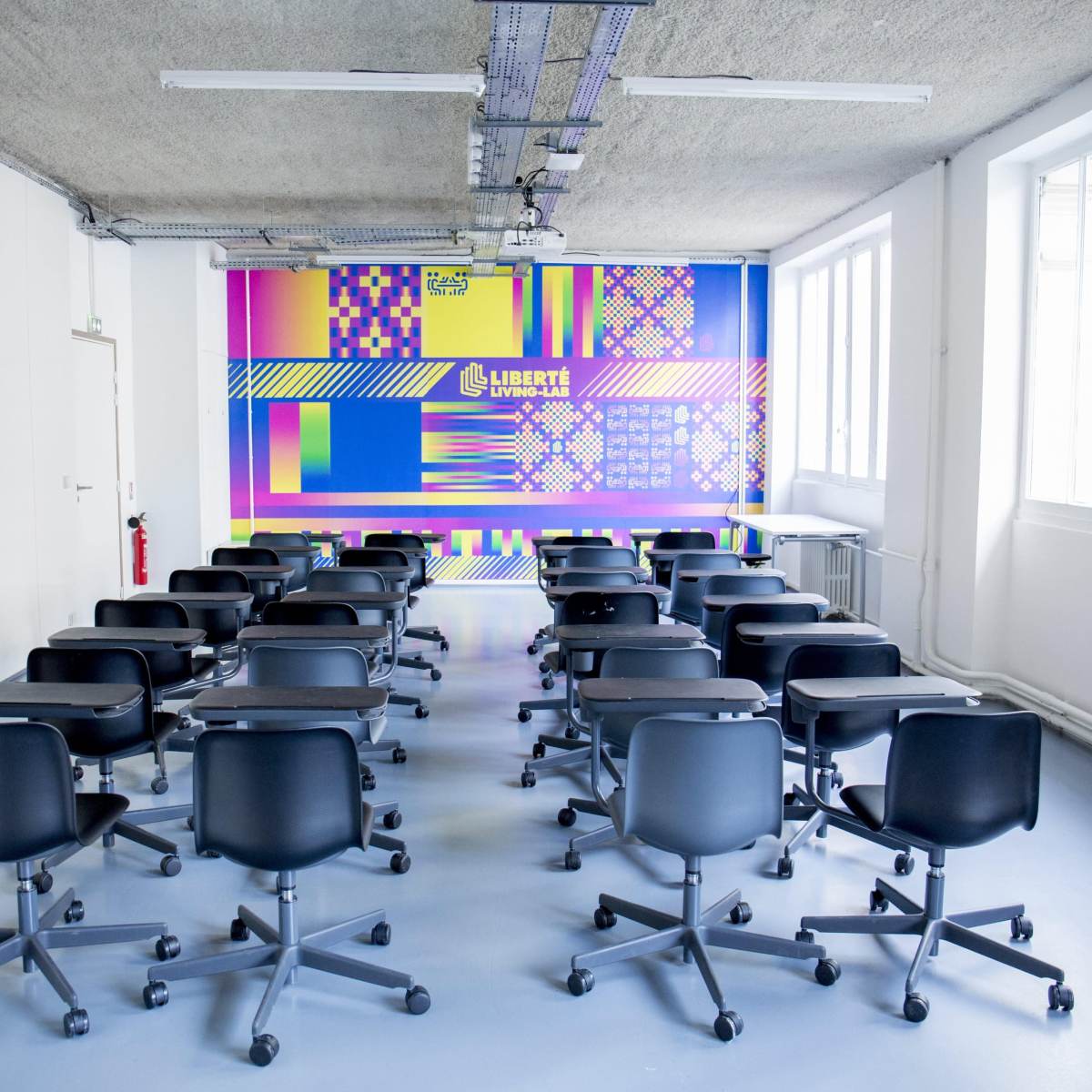 A classroom with multiple black rolling chairs arranged in rows facing a colorful, patterned wall.