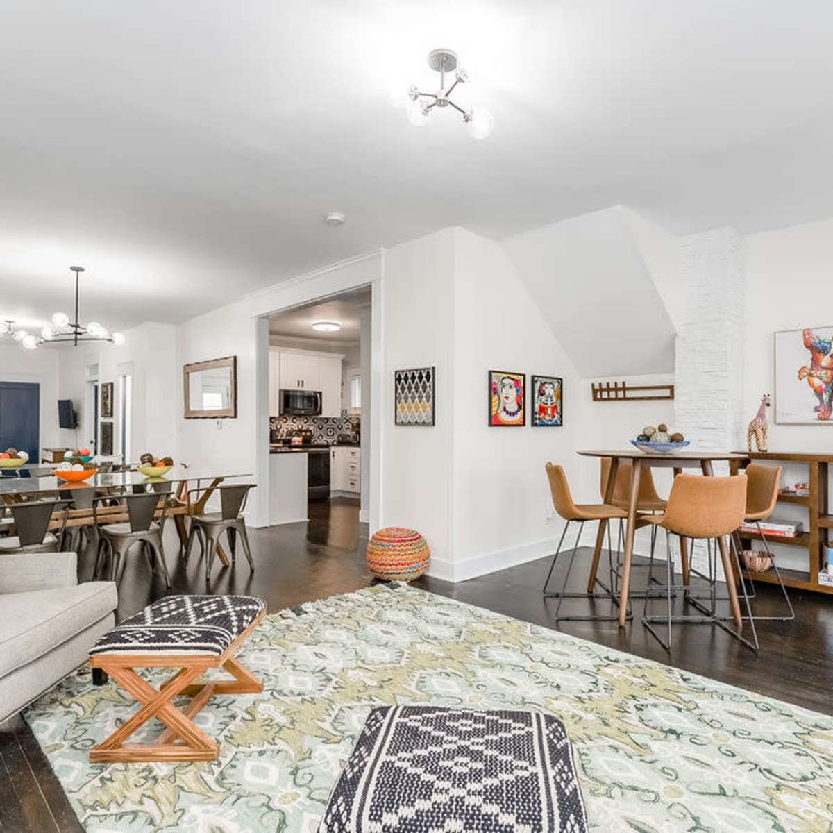 A brightly lit open-plan living space featuring a dining area, a cozy living room, and a modern kitchen in the background.